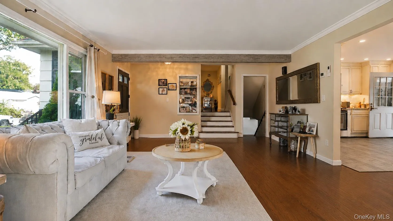 Spacious living area featuring wood-finish flooring, a large window, and crown molding Spacious living area featuring wood-finish flooring, a large window, and crown molding