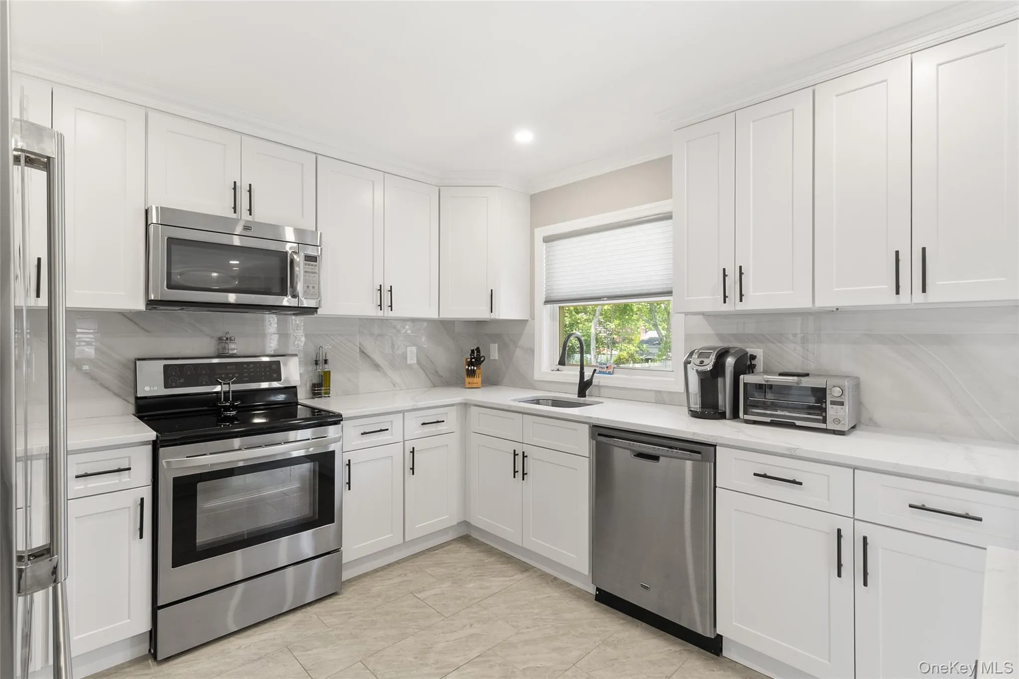 Modern kitchen featuring white shaker-style cabinetry, stainless steel appliances, marble-look countertops, and a coordinating full-height backsplash Modern kitchen featuring white shaker-style cabinetry, stainless steel appliances, marble-look countertops, and a coordinating full-height backsplash