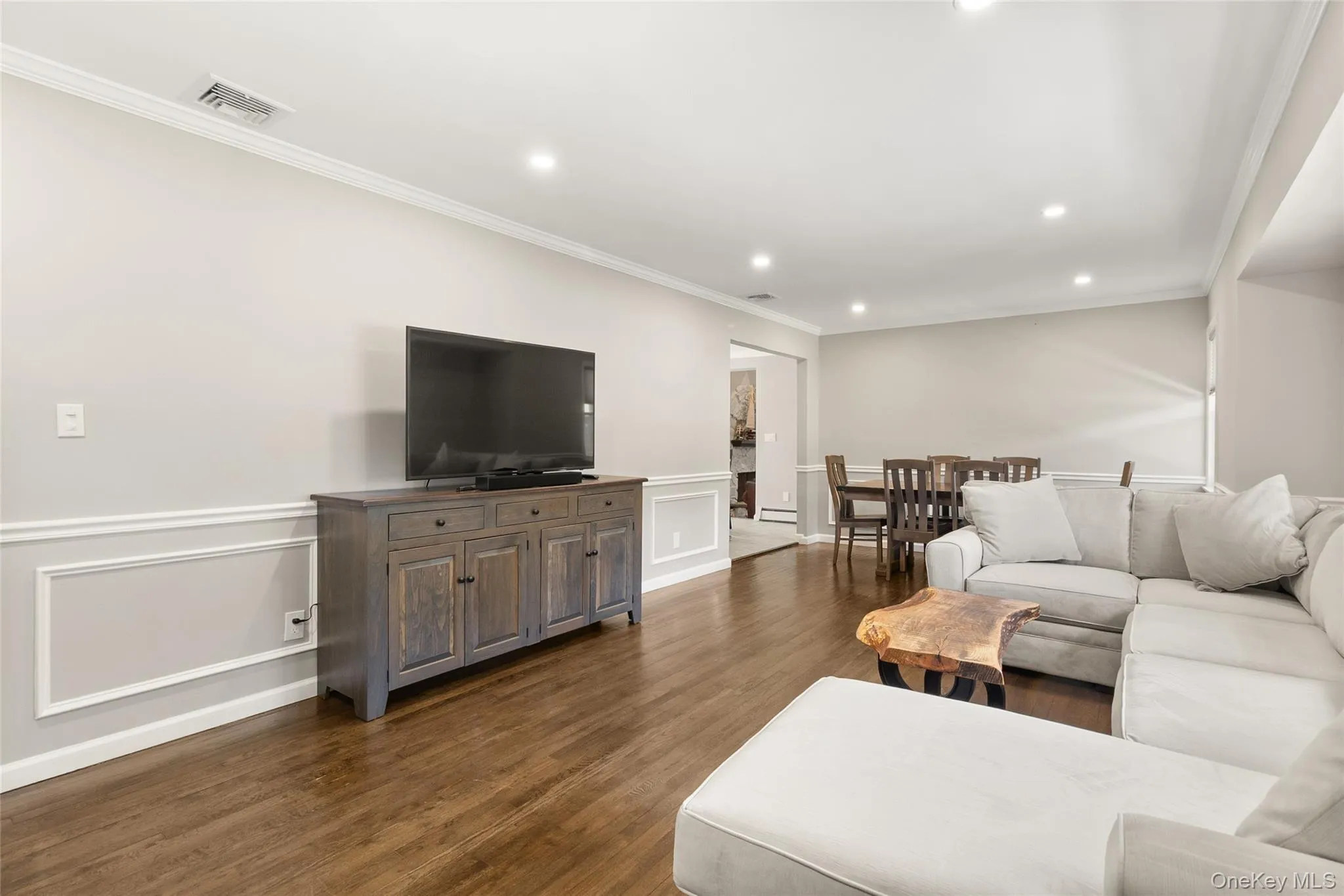 Open-concept living area featuring wood-finish flooring, recessed lighting, crown molding, chair rail with panel molding, and a wide entryway to the dining area Open-concept living area featuring wood-finish flooring, recessed lighting, crown molding, chair rail with panel molding, and a wide entryway to the dining area