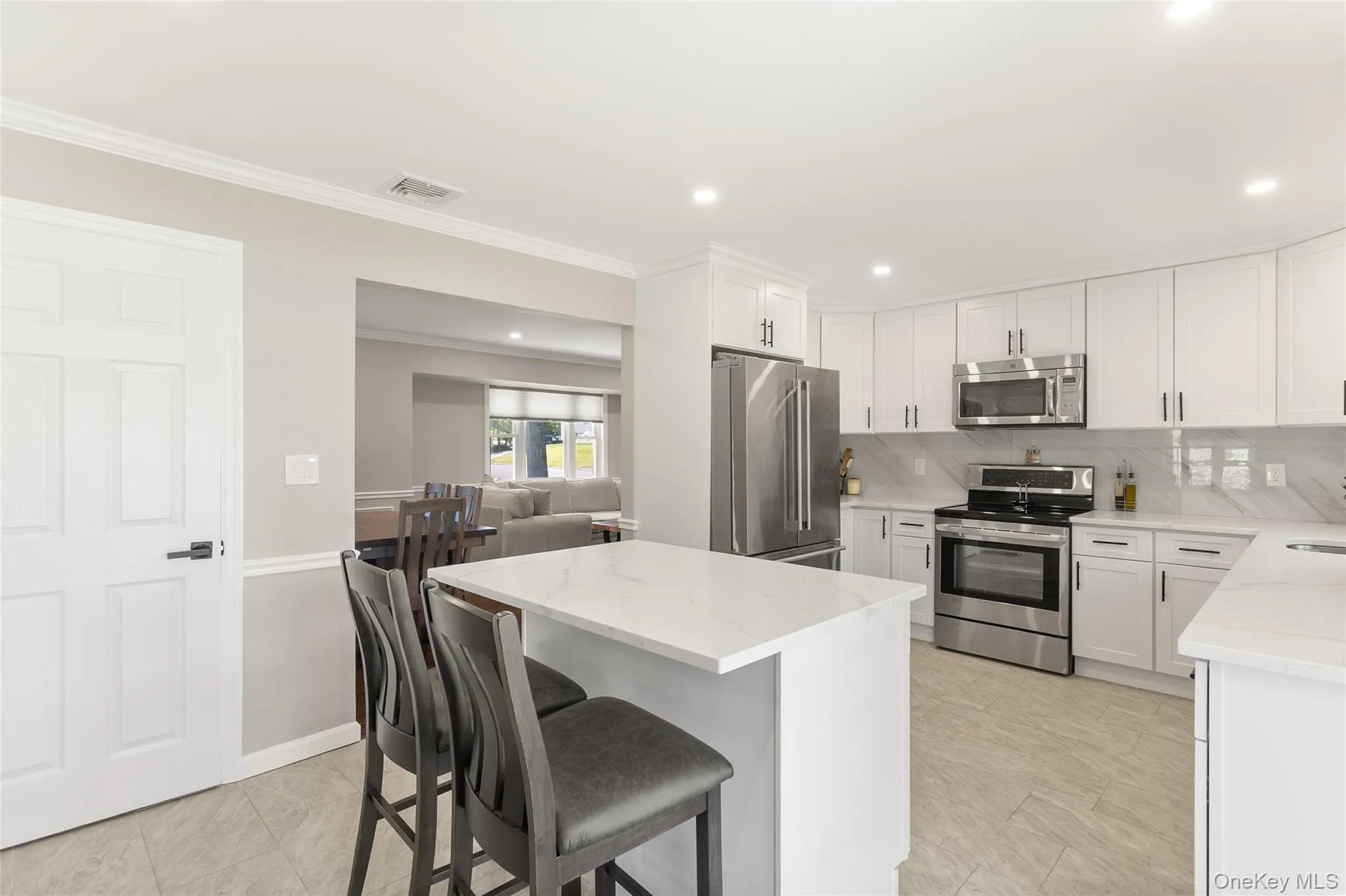 Bright kitchen featuring white cabinetry, stainless steel appliances, a center island with quartz countertop seating. Bright kitchen featuring white cabinetry, stainless steel appliances, a center island with quartz countertop seating.