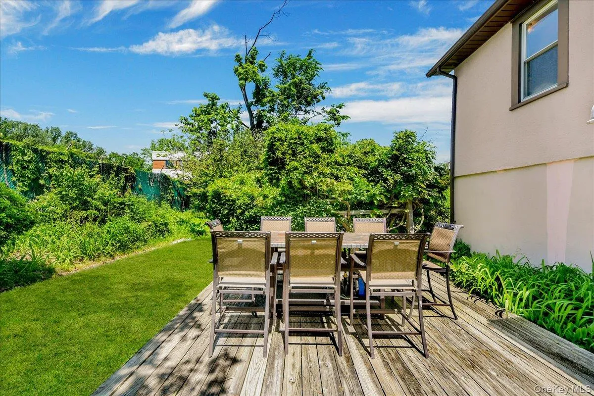 Expansive rear deck with natural wood planks, featuring a manicured lawn and mature perimeter plantings Expansive rear deck with natural wood planks, featuring a manicured lawn and mature perimeter plantings