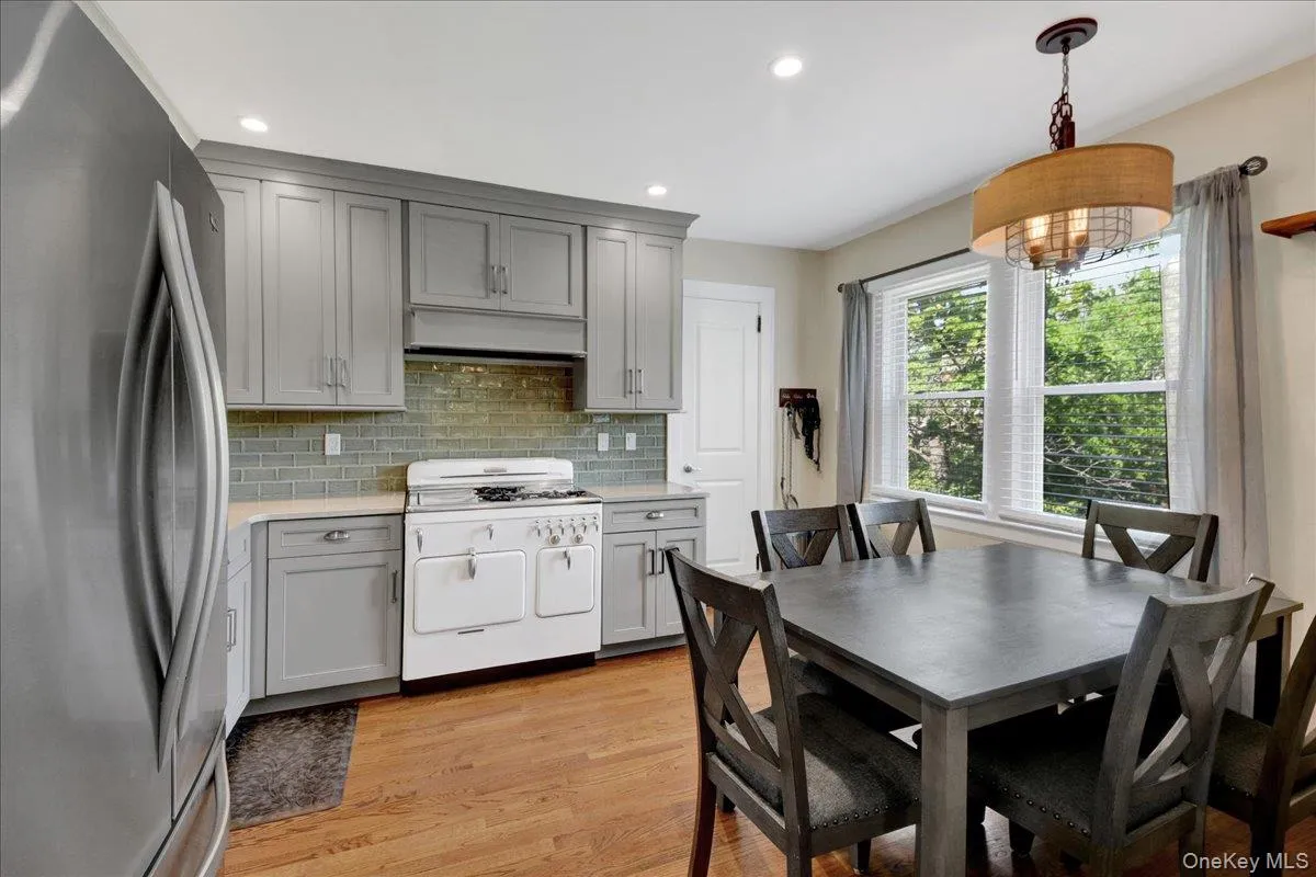 Kitchen and dining area featuring gray shaker cabinetry, light-colored countertops, a subway tile backsplash, and wood-finish flooring Kitchen and dining area featuring gray shaker cabinetry, light-colored countertops, a subway tile backsplash, and wood-finish flooring