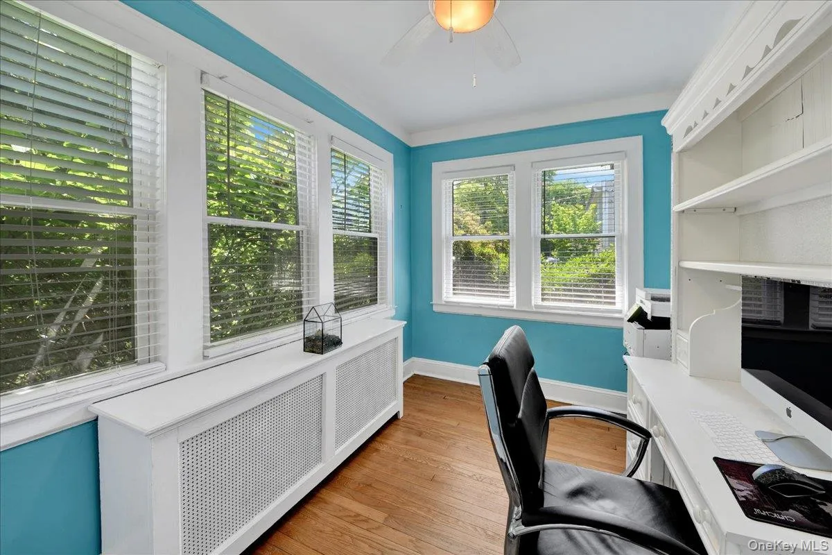 Room featuring wood-finish flooring, multiple windows with blinds, and built-in shelving Room featuring wood-finish flooring, multiple windows with blinds, and built-in shelving