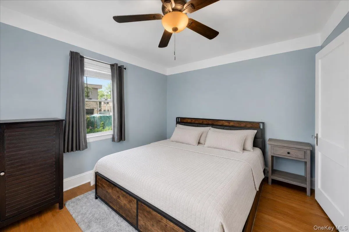 Bedroom with wood-finish flooring, a ceiling fan with integrated lighting, and a white-trimmed window Bedroom with wood-finish flooring, a ceiling fan with integrated lighting, and a white-trimmed window