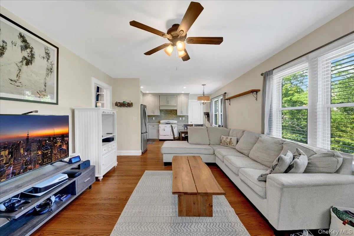 Open-concept living area featuring wood-finish flooring, a ceiling fan with integrated lighting, and multiple windows with blinds Open-concept living area featuring wood-finish flooring, a ceiling fan with integrated lighting, and multiple windows with blinds