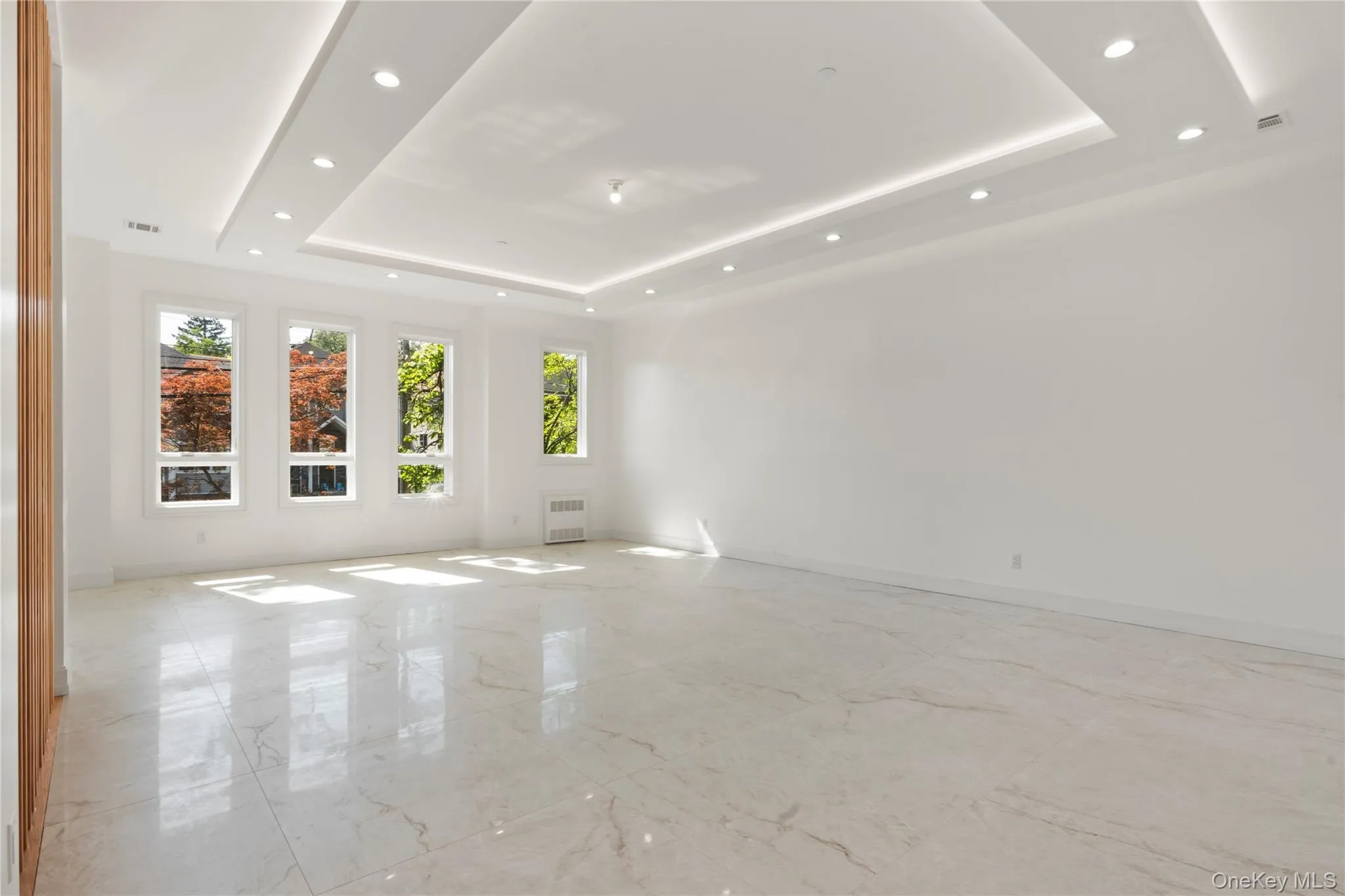 Spare room with light marble finish floors, a tray ceiling, recessed lighting, and radiator Spare room with light marble finish floors, a tray ceiling, recessed lighting, and radiator