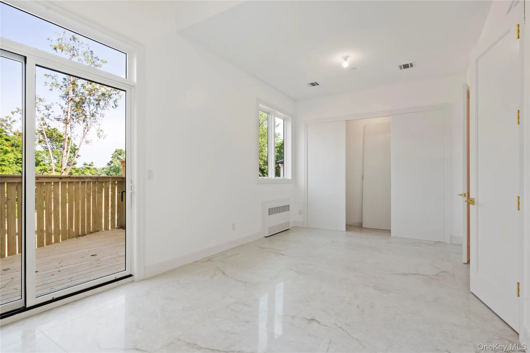 Unfurnished bedroom featuring light marble finish floors, radiator heating unit, and access to outside Unfurnished bedroom featuring light marble finish floors, radiator heating unit, and access to outside