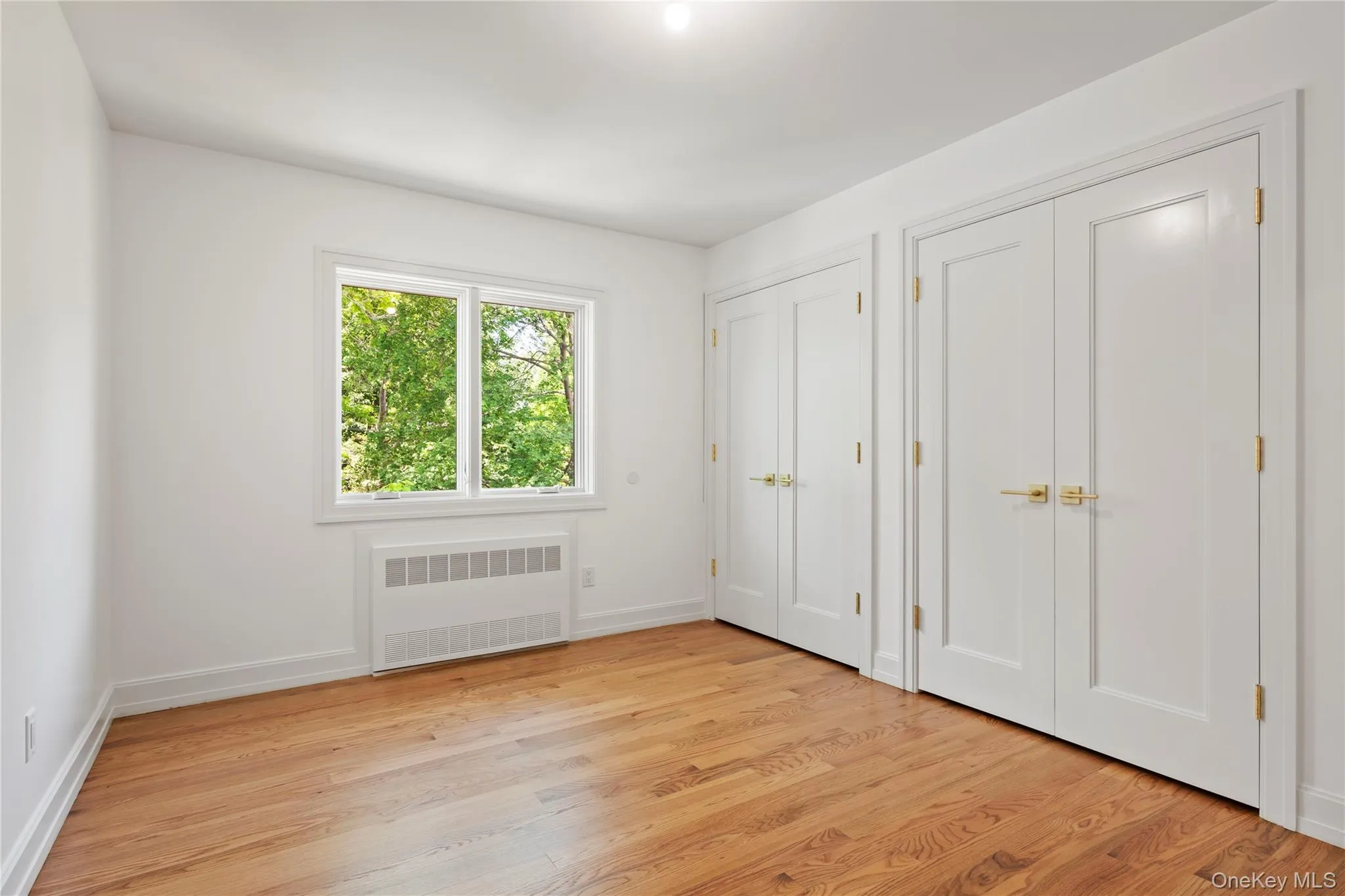 Unfurnished bedroom featuring two closets, radiator, and light wood finished floors Unfurnished bedroom featuring two closets, radiator, and light wood finished floors