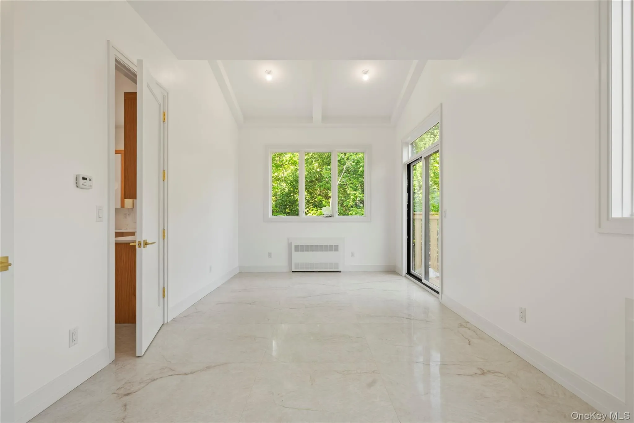Empty room with beamed ceiling, light marble finish floors, and radiator heating unit Empty room with beamed ceiling, light marble finish floors, and radiator heating unit