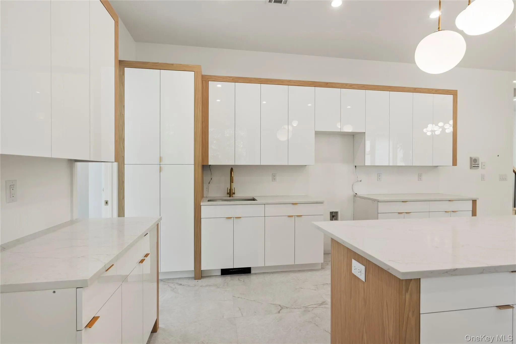 Kitchen featuring white cabinets, light stone countertops, light marble finish flooring, and hanging light fixtures Kitchen featuring white cabinets, light stone countertops, light marble finish flooring, and hanging light fixtures