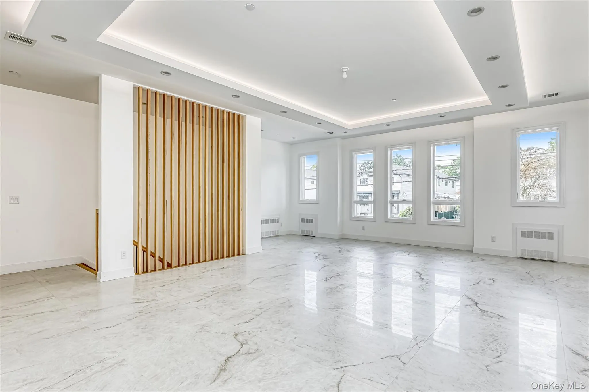 Empty room with a tray ceiling, light marble finish flooring, and radiator heating unit Empty room with a tray ceiling, light marble finish flooring, and radiator heating unit