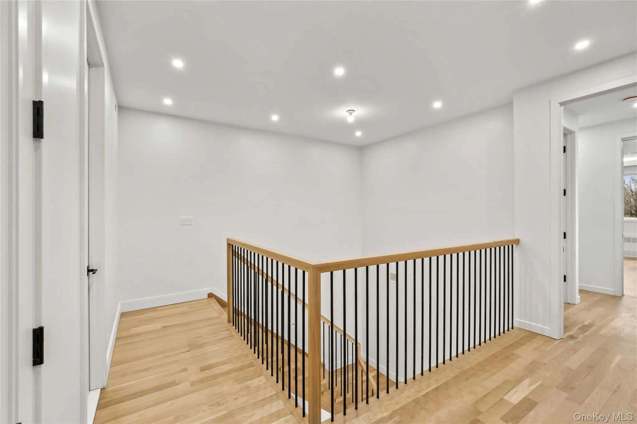Upper-level hallway featuring light wood-finish flooring, recessed lighting, and a contemporary railing with black balusters and a wood handrail Upper-level hallway featuring light wood-finish flooring, recessed lighting, and a contemporary railing with black balusters and a wood handrail