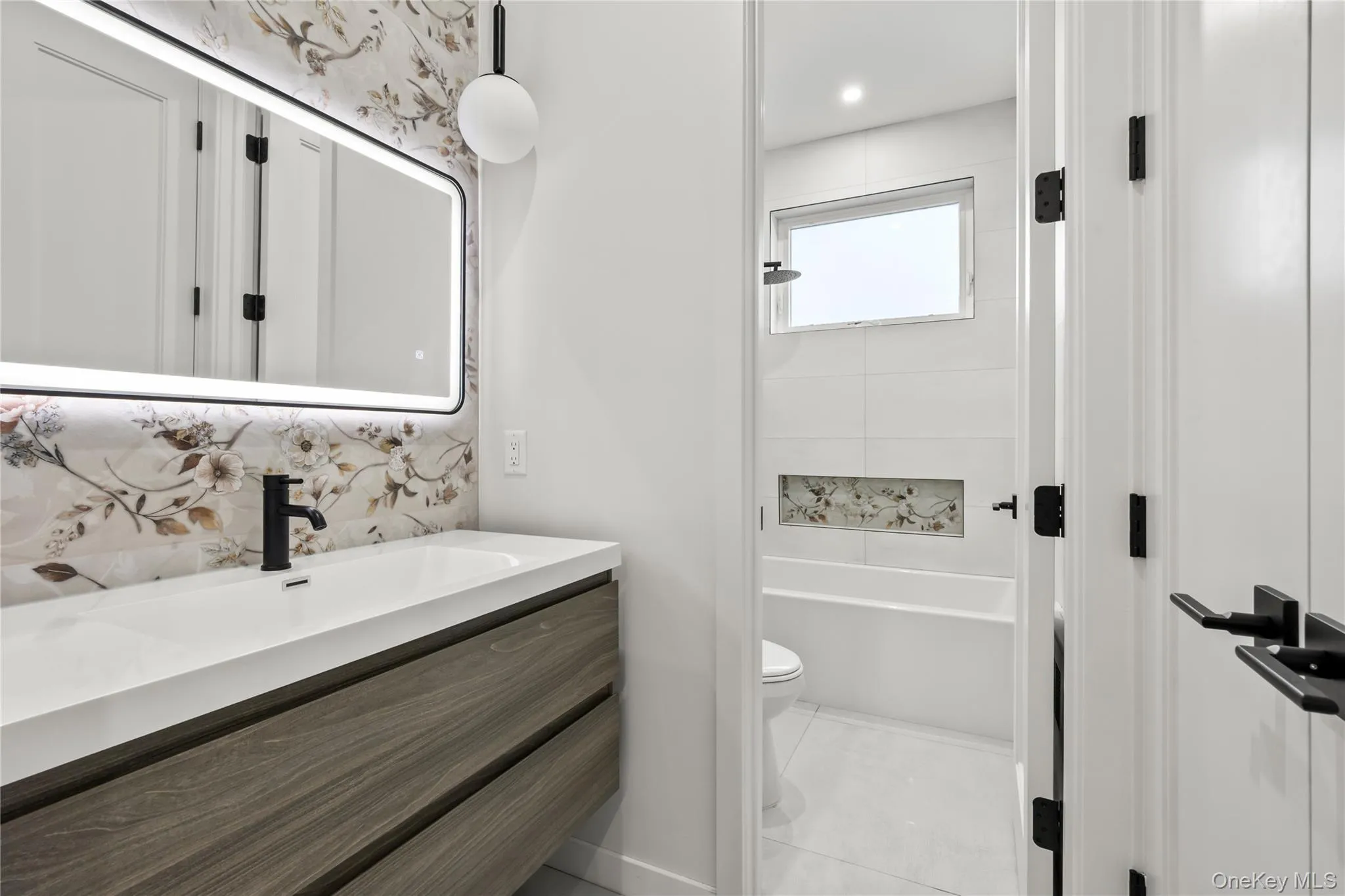 Modern bathroom featuring a floating wood-finish vanity with an integrated sink, a rectangular illuminated mirror, and a contemporary spherical pendant light, designer tiles, and expensive plumbing fixtures Modern bathroom featuring a floating wood-finish vanity with an integrated sink, a rectangular illuminated mirror, and a contemporary spherical pendant light, designer tiles, and expensive plumbing fixtures