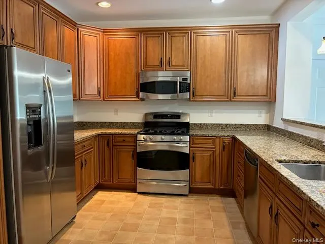 Kitchen featuring full complement of stainless steel appliances, abundant wood cabinetry, granite countertops, tile flooring, and recessed lighting Kitchen featuring full complement of stainless steel appliances, abundant wood cabinetry, granite countertops, tile flooring, and recessed lighting