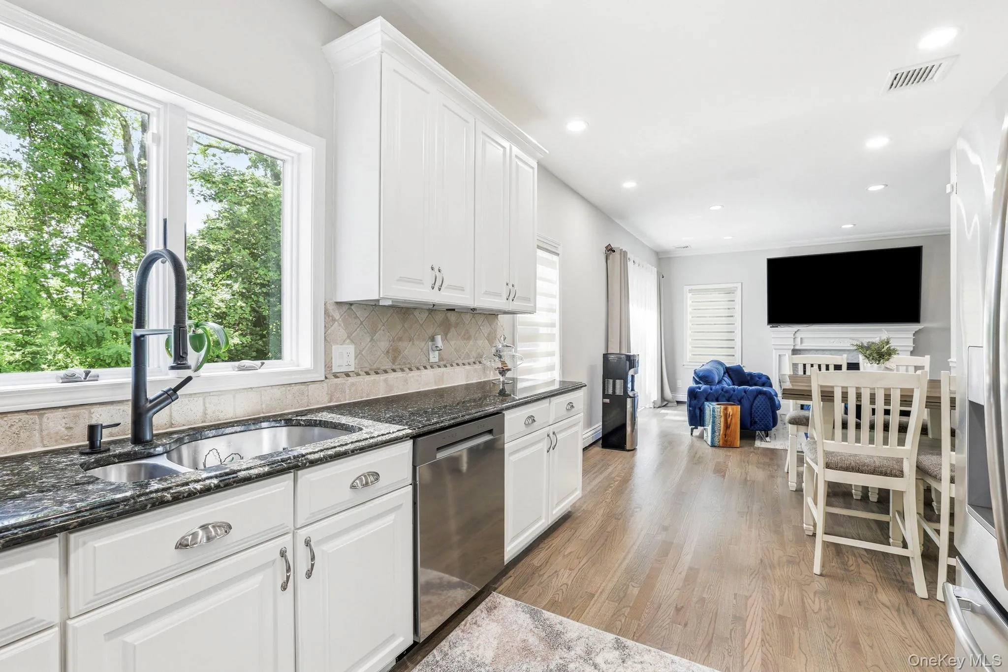 Modern kitchen space featuring white cabinetry, dark granite countertops, and a tile backsplash Modern kitchen space featuring white cabinetry, dark granite countertops, and a tile backsplash