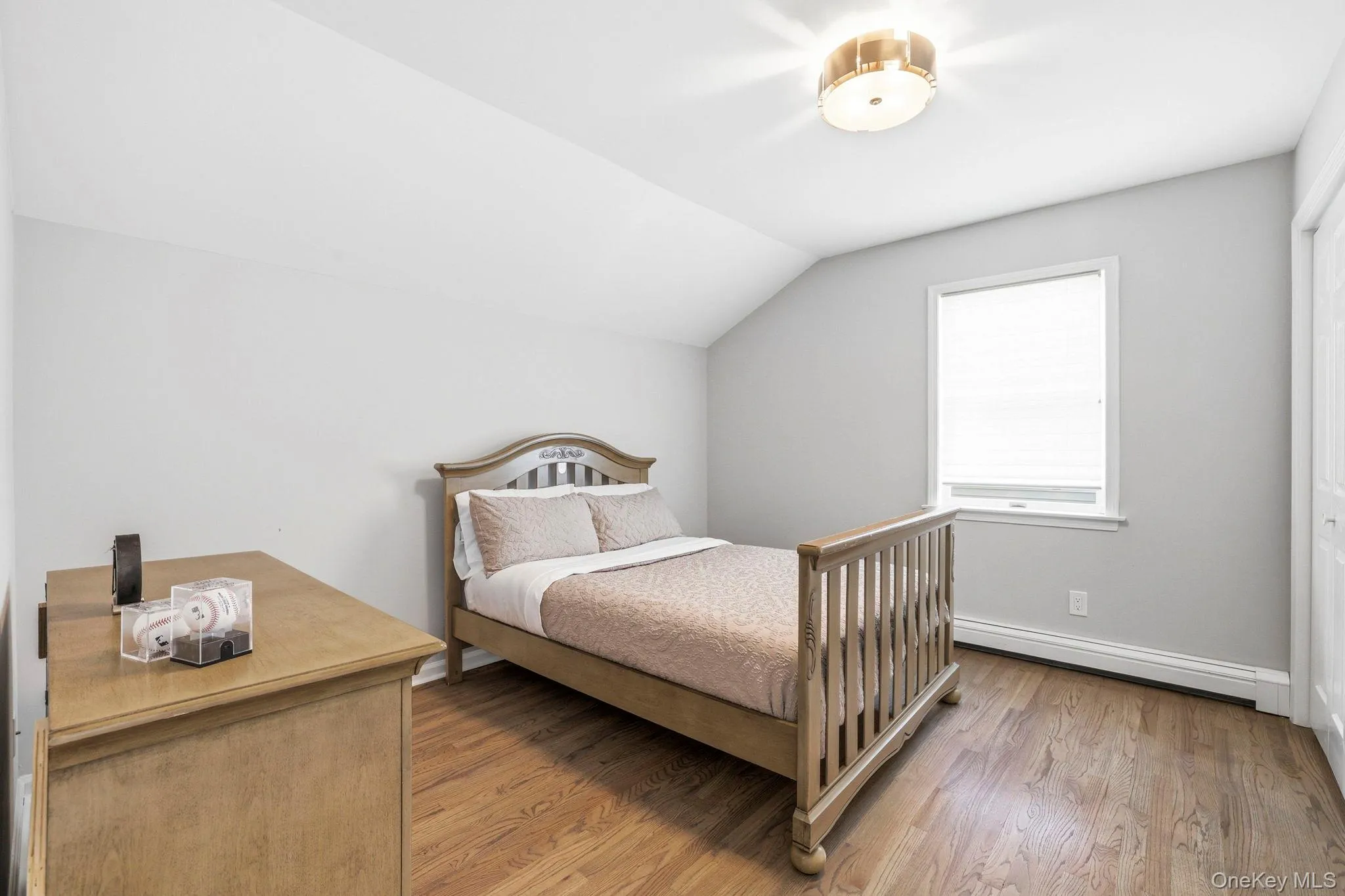 Bedroom featuring wood-finish flooring, a white-framed window, and a flush-mount ceiling light fixture Bedroom featuring wood-finish flooring, a white-framed window, and a flush-mount ceiling light fixture