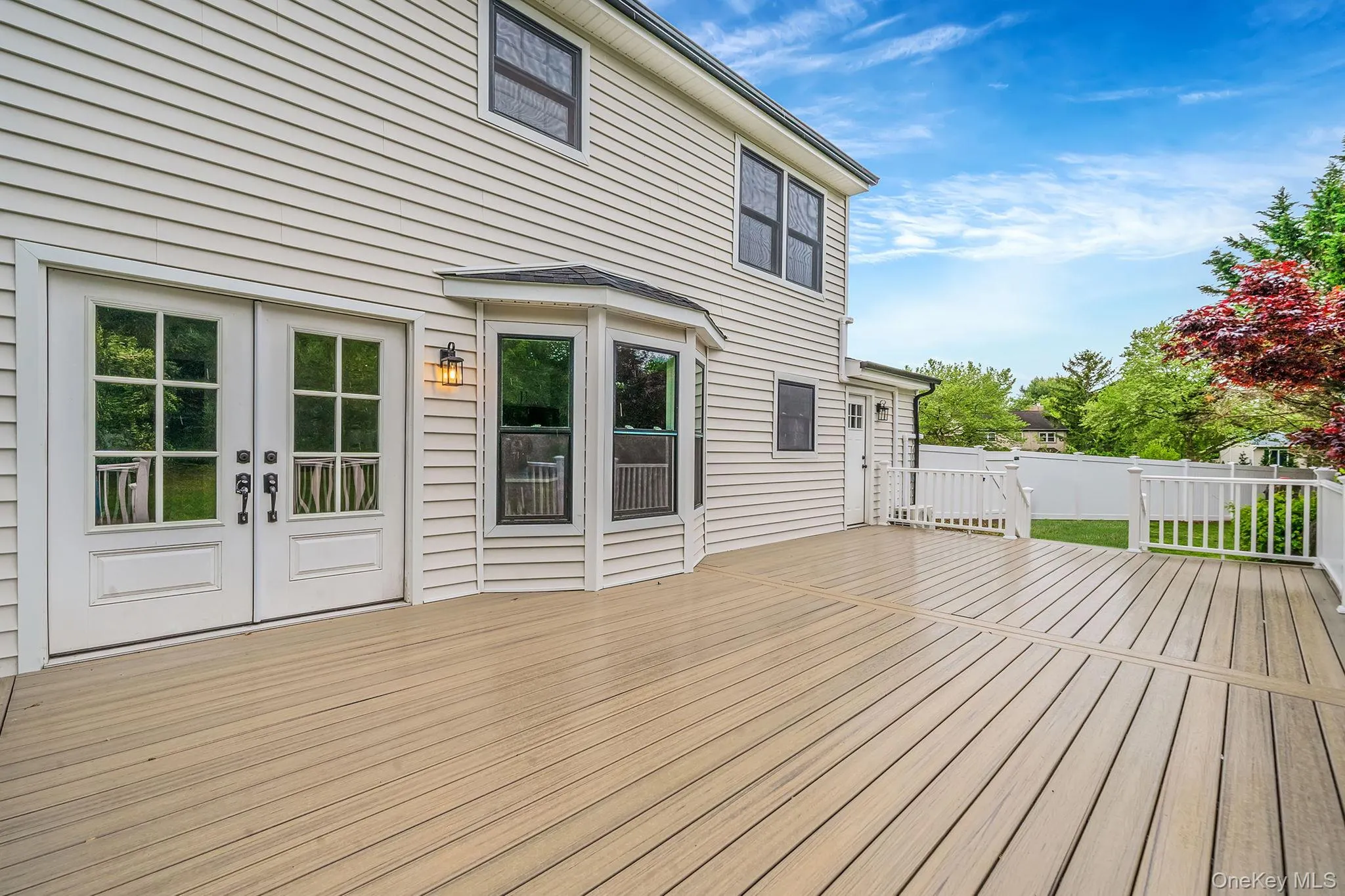 Expansive outdoor deck featuring wood-finish decking, white vinyl siding, and a bay window Expansive outdoor deck featuring wood-finish decking, white vinyl siding, and a bay window