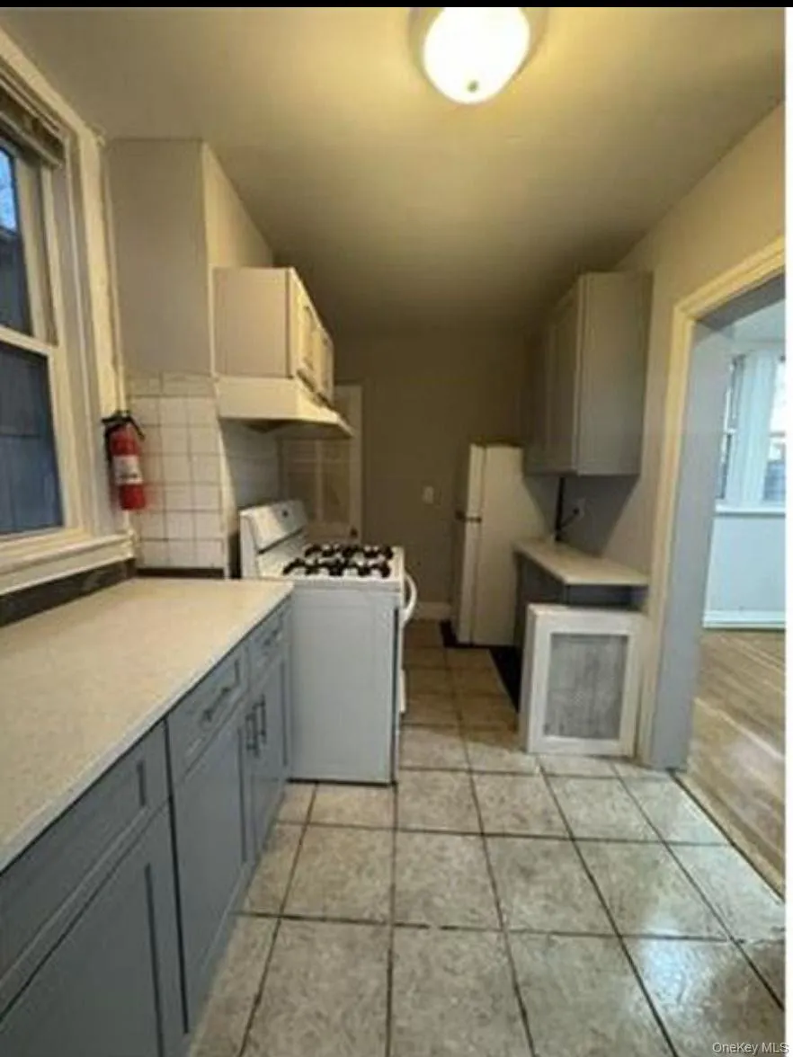 Kitchen featuring light gray base cabinetry, white countertops, tile flooring, a window with natural light, and overhead lighting Kitchen featuring light gray base cabinetry, white countertops, tile flooring, a window with natural light, and overhead lighting