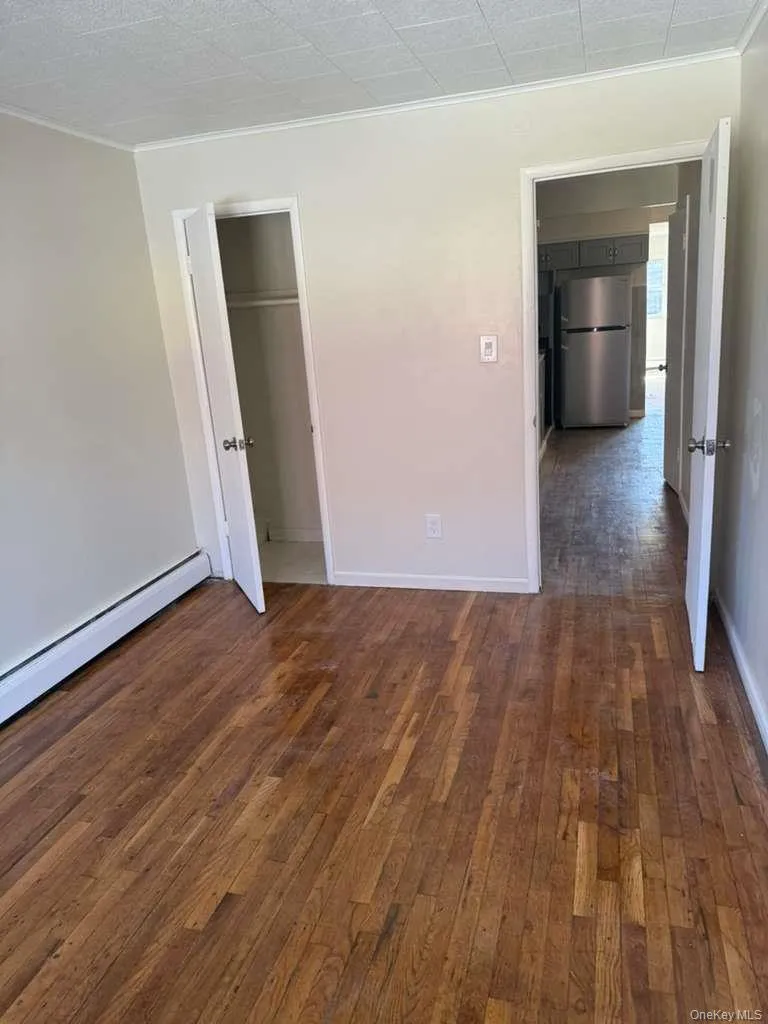Room featuring wood-finish flooring, light-toned wall paint, and white baseboard trim Room featuring wood-finish flooring, light-toned wall paint, and white baseboard trim