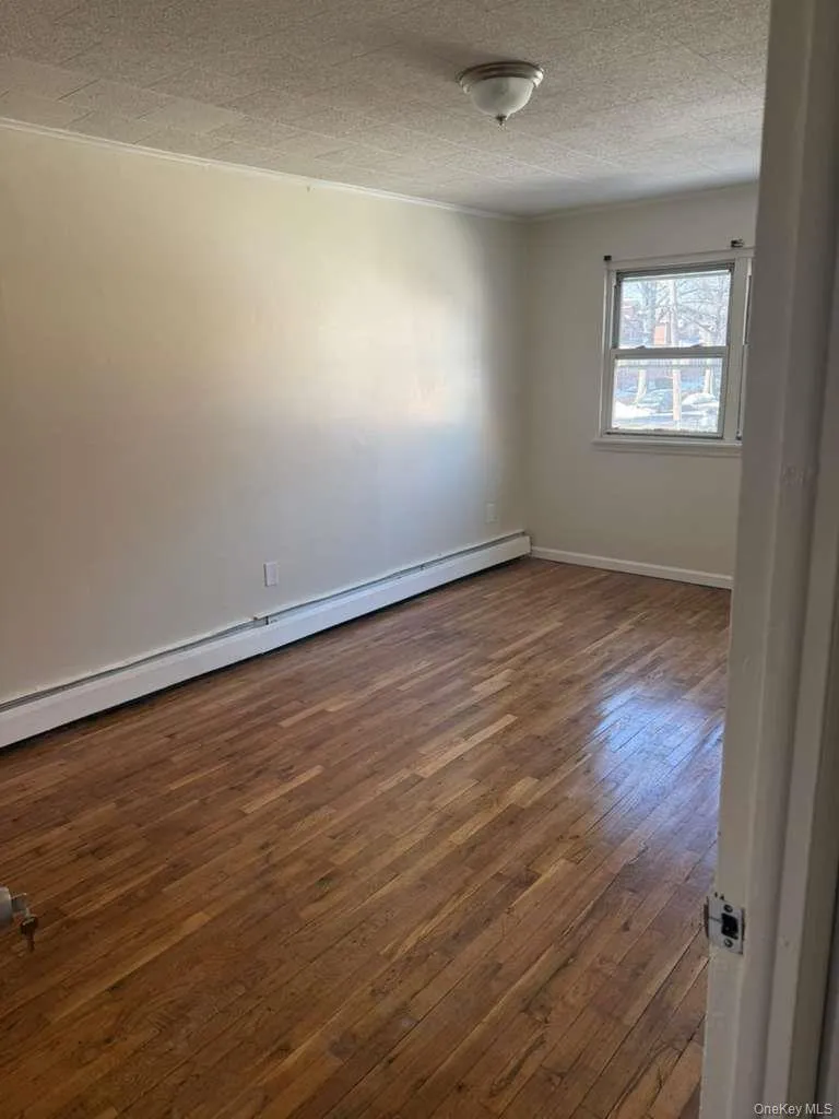 Hardwood flooring spanning the room, white baseboards, and a single window with trim Hardwood flooring spanning the room, white baseboards, and a single window with trim