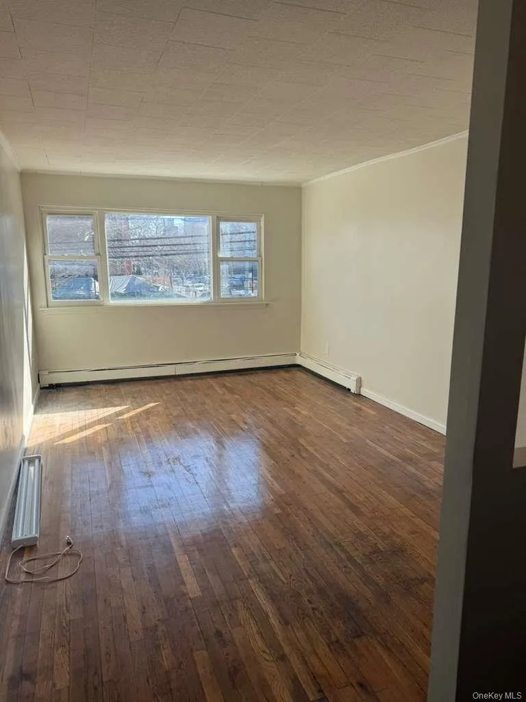 Hardwood flooring throughout a room featuring multiple windows, baseboard heating, and light-toned walls Hardwood flooring throughout a room featuring multiple windows, baseboard heating, and light-toned walls