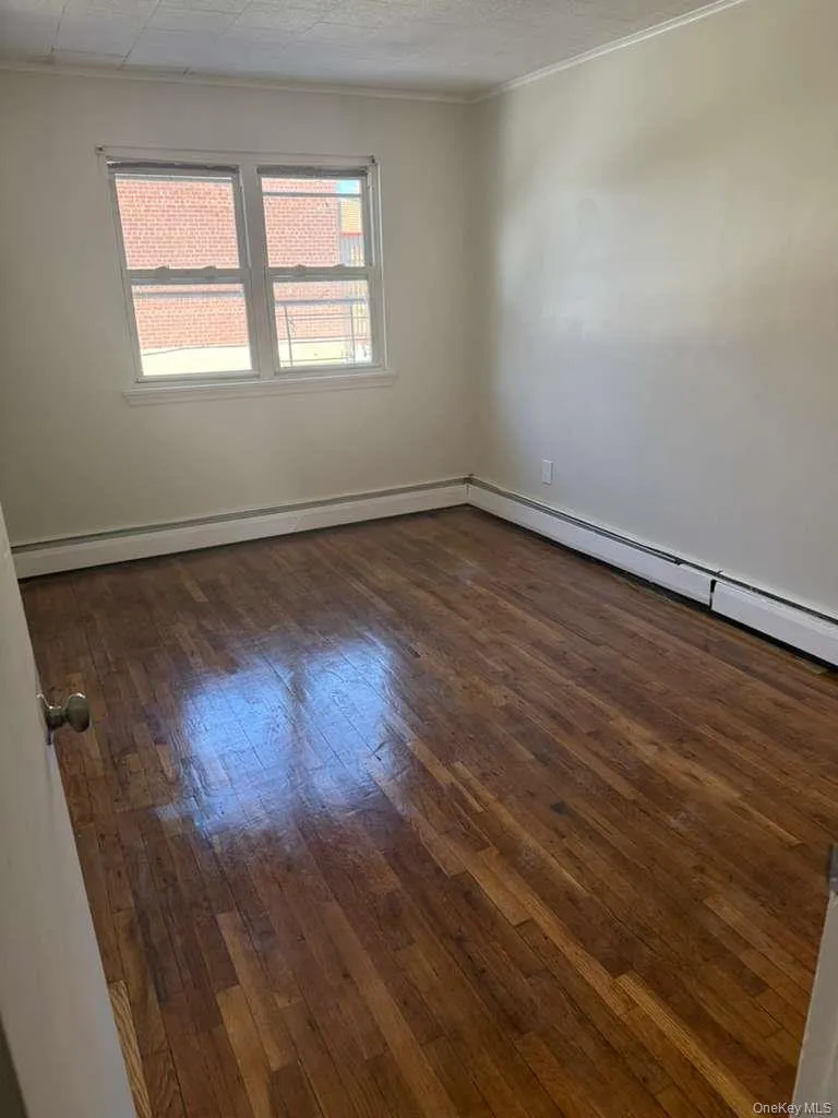 Bright interior space featuring wood-finish flooring, white baseboards, and a large window with white trim Bright interior space featuring wood-finish flooring, white baseboards, and a large window with white trim