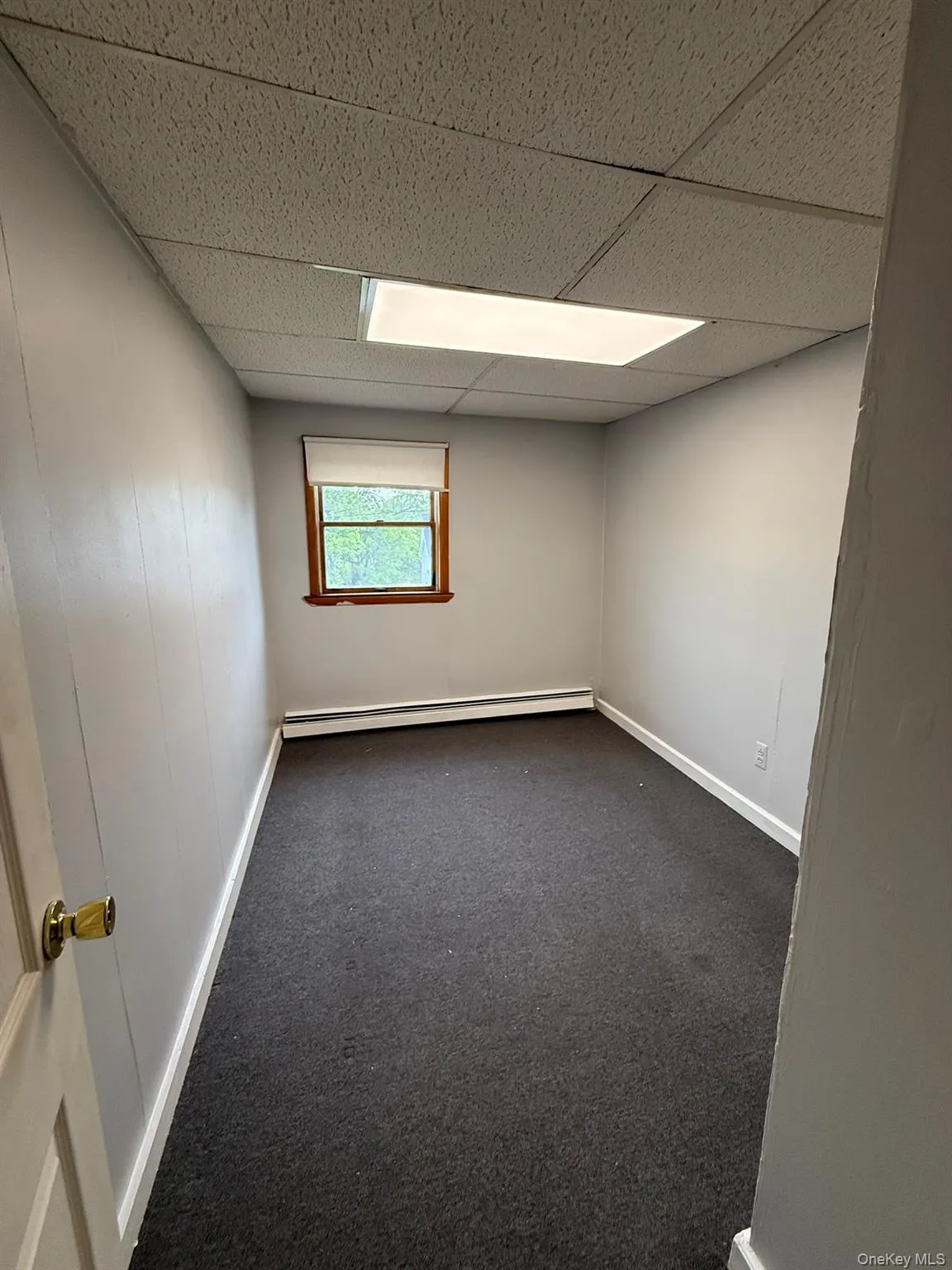 Compact room featuring neutral gray walls and dark gray carpeting Compact room featuring neutral gray walls and dark gray carpeting
