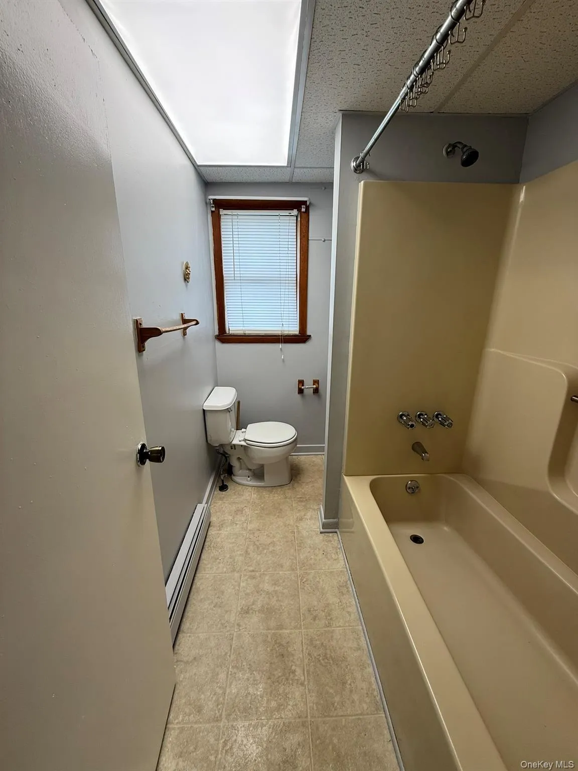 Bathroom featuring a combined shower and tub unit, a toilet, a window with wood trim, and tile-look flooring Bathroom featuring a combined shower and tub unit, a toilet, a window with wood trim, and tile-look flooring