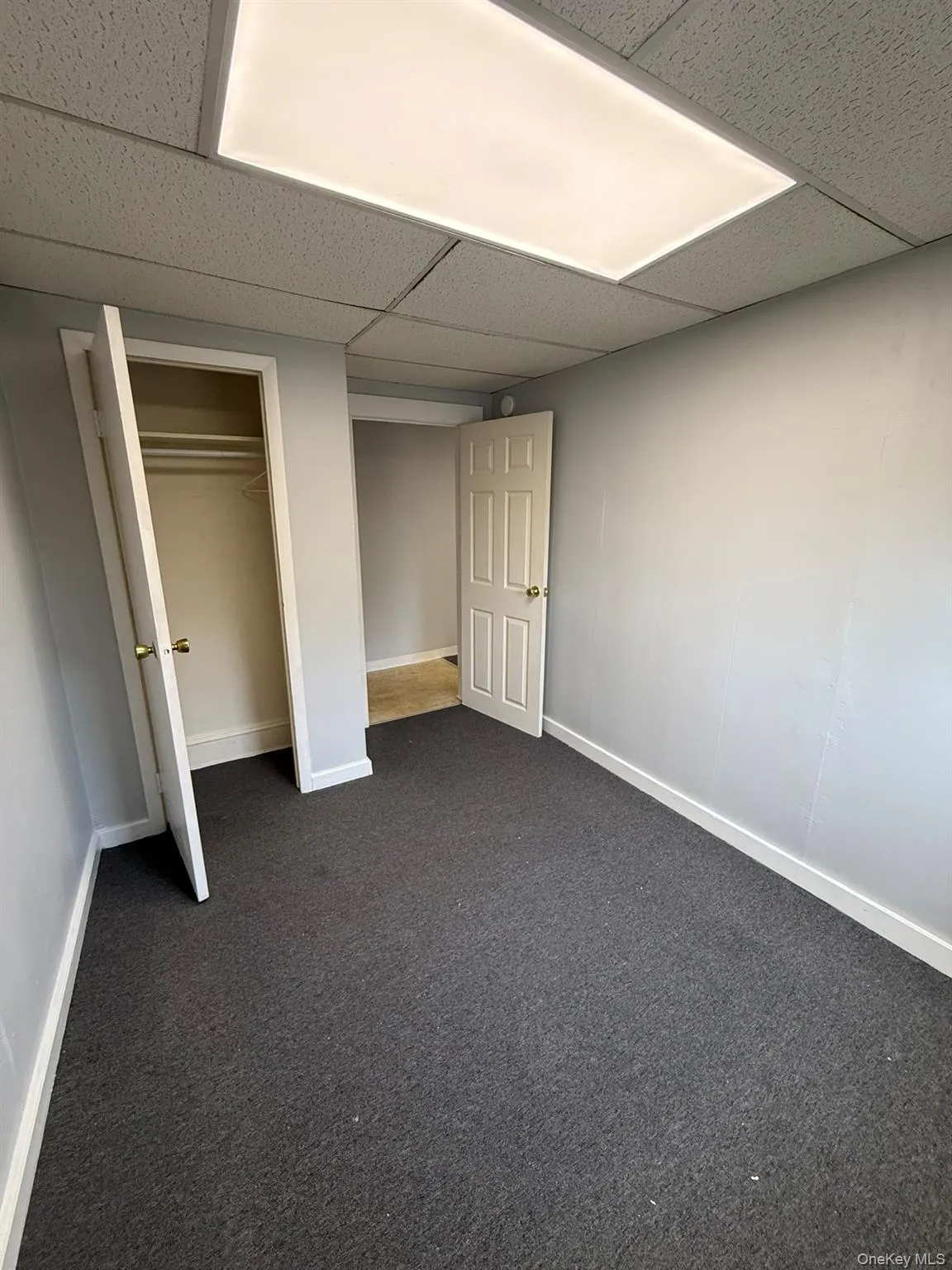 Room featuring dark grey carpeting, light grey painted walls, and white baseboards Room featuring dark grey carpeting, light grey painted walls, and white baseboards