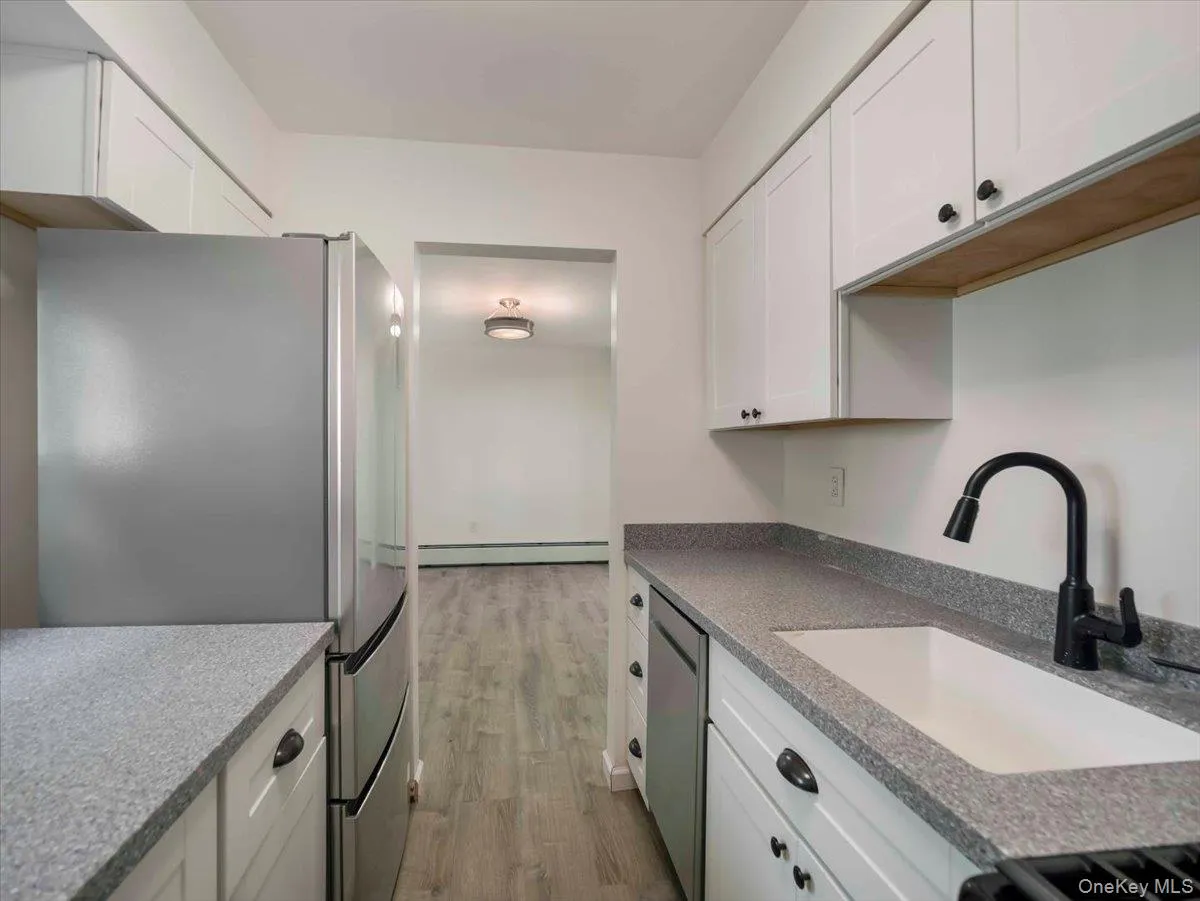 Galley kitchen featuring white cabinetry, speckled countertops, stainless steel appliances, a deep single-basin sink, and a matte black gooseneck faucet Galley kitchen featuring white cabinetry, speckled countertops, stainless steel appliances, a deep single-basin sink, and a matte black gooseneck faucet