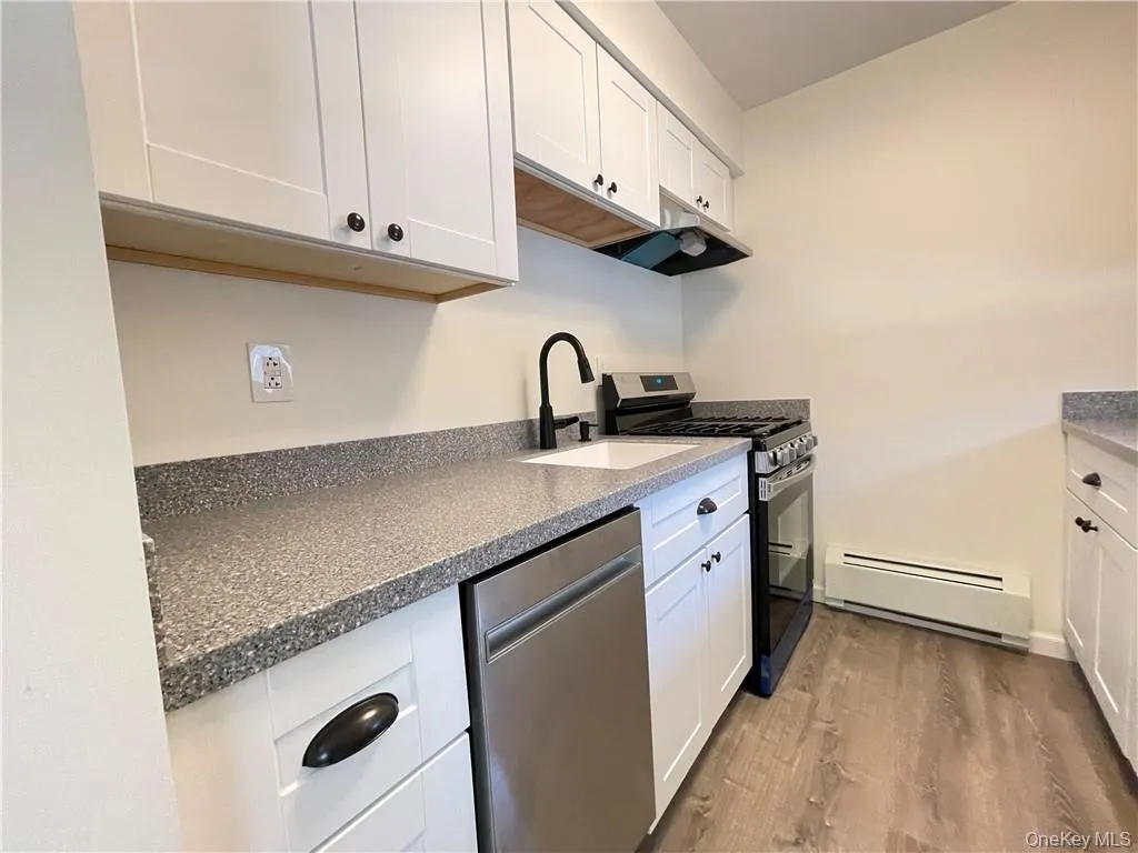 Kitchen featuring white shaker cabinetry, speckled countertops, a stainless steel dishwasher, a gas range with an overhead vent, and wood-finish flooring Kitchen featuring white shaker cabinetry, speckled countertops, a stainless steel dishwasher, a gas range with an overhead vent, and wood-finish flooring