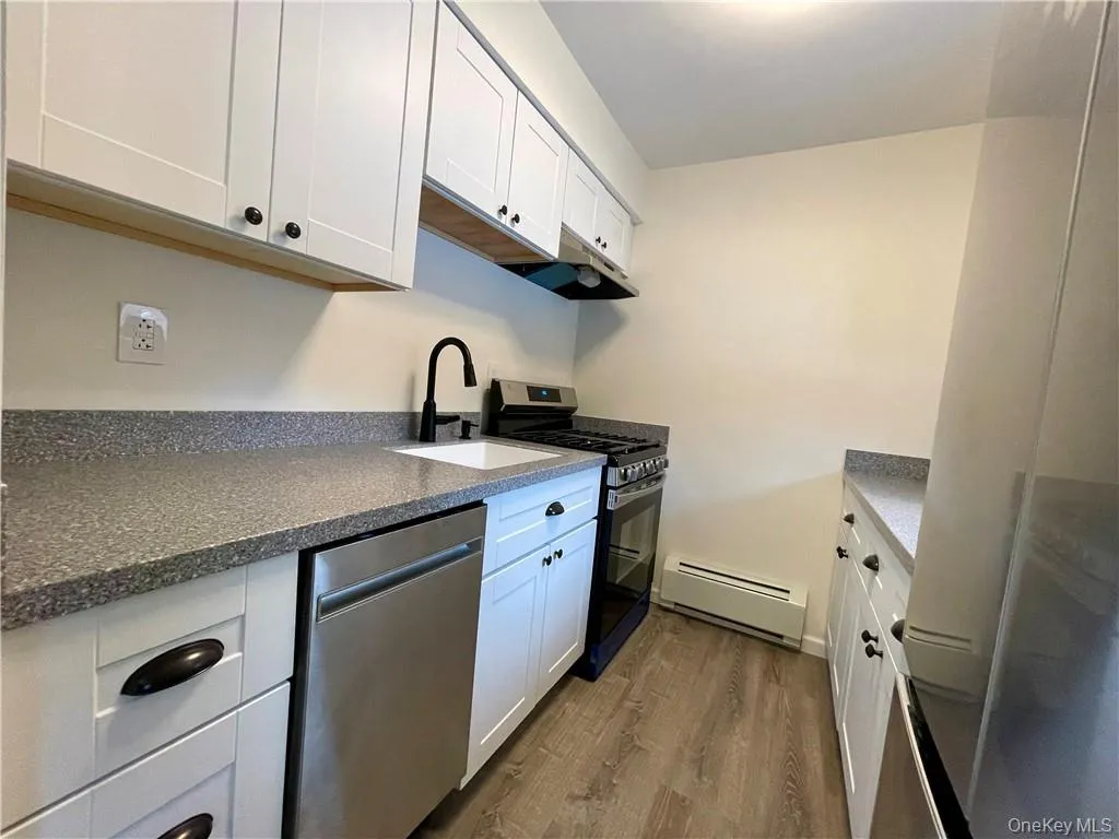 Modern kitchen featuring white shaker cabinetry with dark hardware, speckled countertops, a stainless steel dishwasher, and a gas range Modern kitchen featuring white shaker cabinetry with dark hardware, speckled countertops, a stainless steel dishwasher, and a gas range