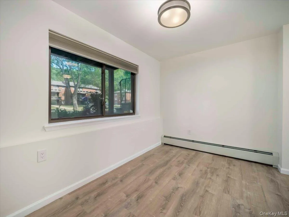 Room featuring wood-finish flooring, white painted walls, and a window with a roller shade Room featuring wood-finish flooring, white painted walls, and a window with a roller shade