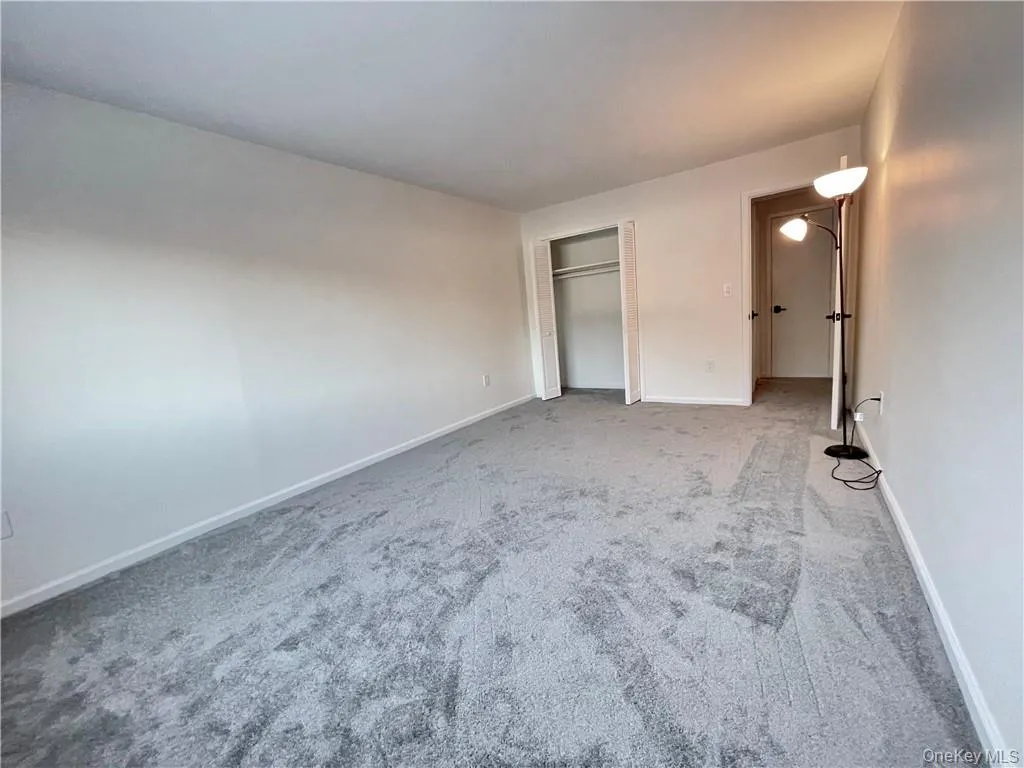Spacious room featuring gray wall-to-wall carpeting, white baseboards, and a built-in closet with a clothes rod Spacious room featuring gray wall-to-wall carpeting, white baseboards, and a built-in closet with a clothes rod