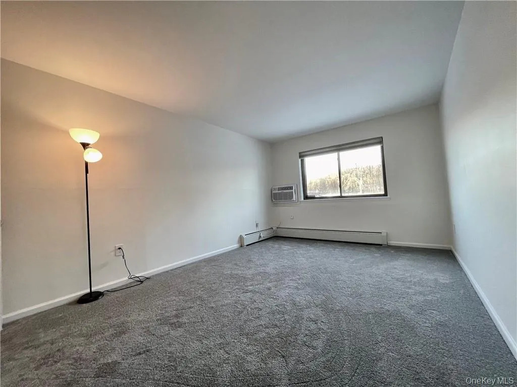 Spacious room featuring gray carpet, white walls, and a large window Spacious room featuring gray carpet, white walls, and a large window