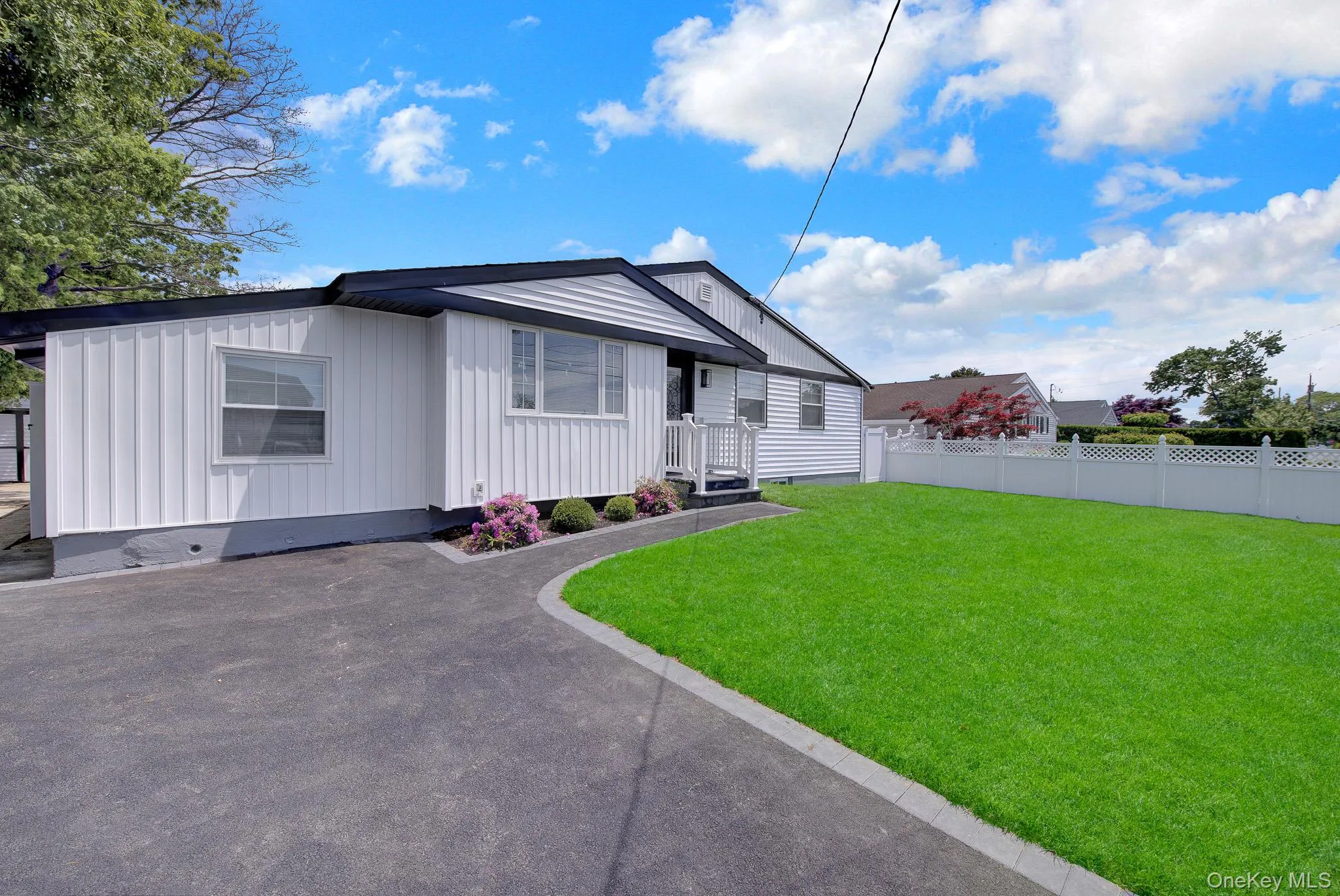 White siding exterior with dark trim accents, featuring a paved driveway, a manicured lawn, and low-maintenance landscaping White siding exterior with dark trim accents, featuring a paved driveway, a manicured lawn, and low-maintenance landscaping