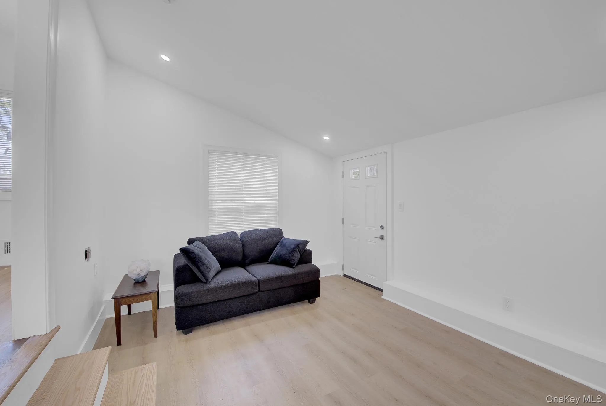 Interior room featuring wood-finish flooring, white walls, and a white paneled entry door Interior room featuring wood-finish flooring, white walls, and a white paneled entry door