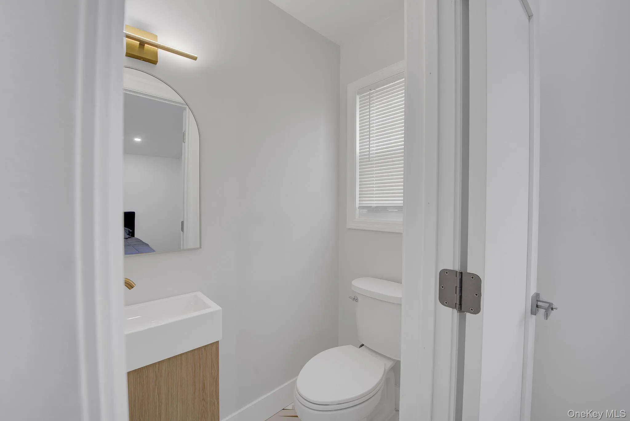 Powder room featuring a sleek arched mirror, contemporary brass-finish sconce, and a floating wood-finish vanity with an integrated sink Powder room featuring a sleek arched mirror, contemporary brass-finish sconce, and a floating wood-finish vanity with an integrated sink