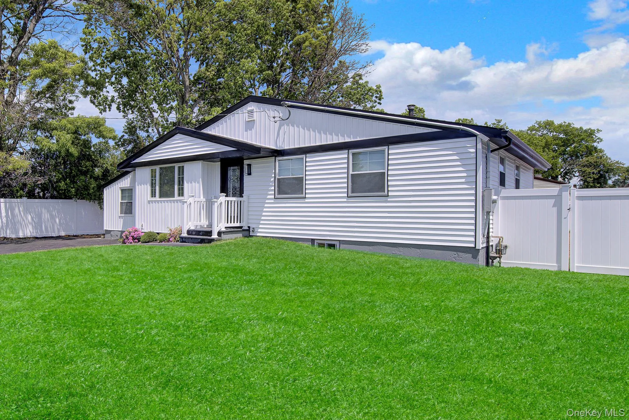 White siding residence featuring black trim, a front entry with a white railing, a manicured lawn, and a white privacy fence White siding residence featuring black trim, a front entry with a white railing, a manicured lawn, and a white privacy fence