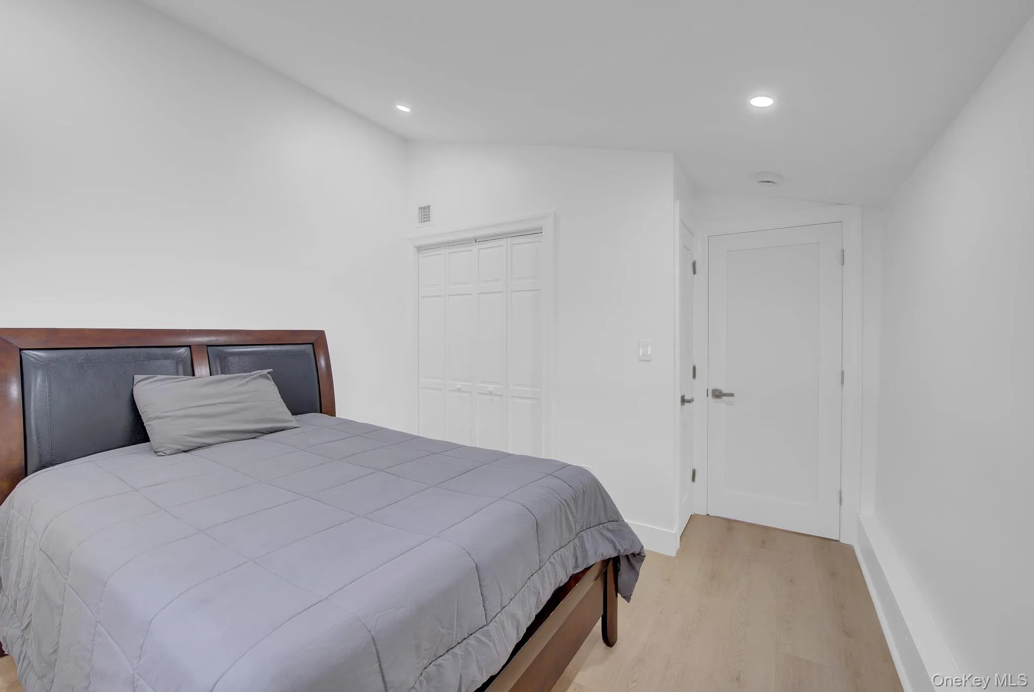 Bedroom featuring light wood-finish flooring, recessed lighting, white walls, and a closet with bifold doors Bedroom featuring light wood-finish flooring, recessed lighting, white walls, and a closet with bifold doors