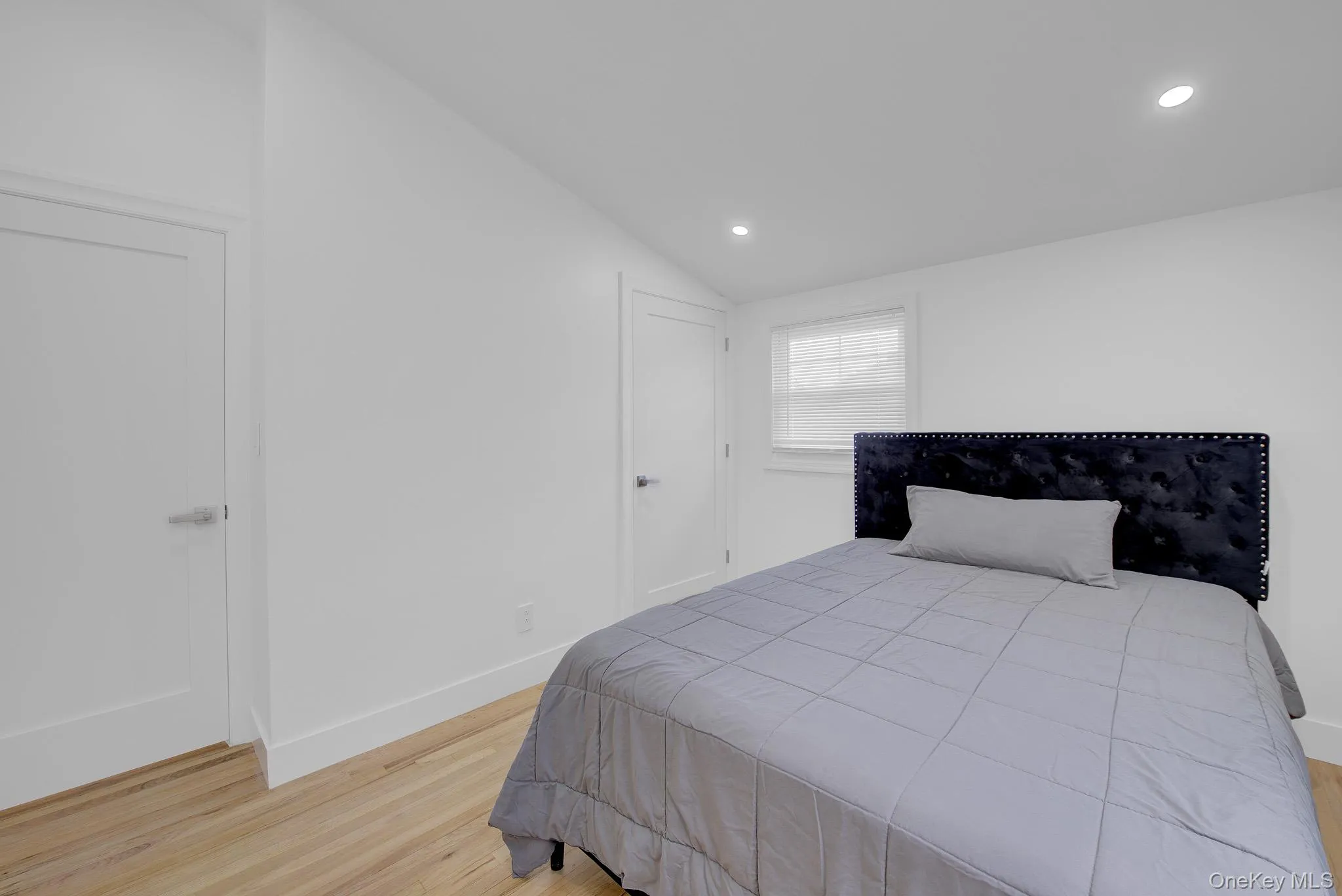 Bedroom featuring hardwood flooring, recessed lighting, white walls, and a window with blinds Bedroom featuring hardwood flooring, recessed lighting, white walls, and a window with blinds