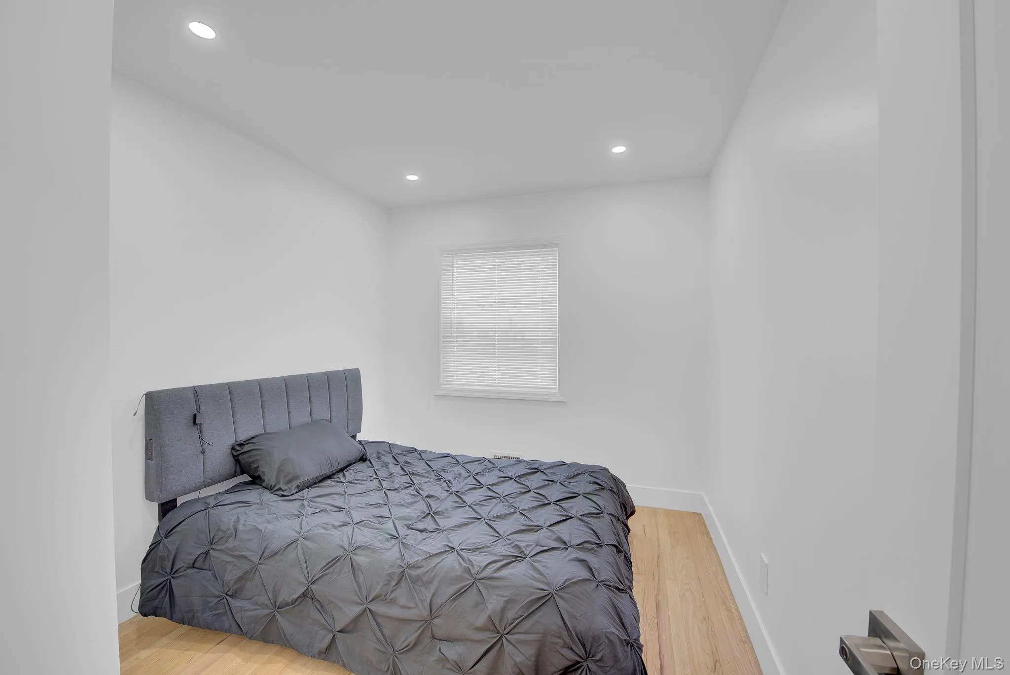 Bright room featuring recessed lighting, a window with blinds, wood-finish flooring, and white baseboards Bright room featuring recessed lighting, a window with blinds, wood-finish flooring, and white baseboards