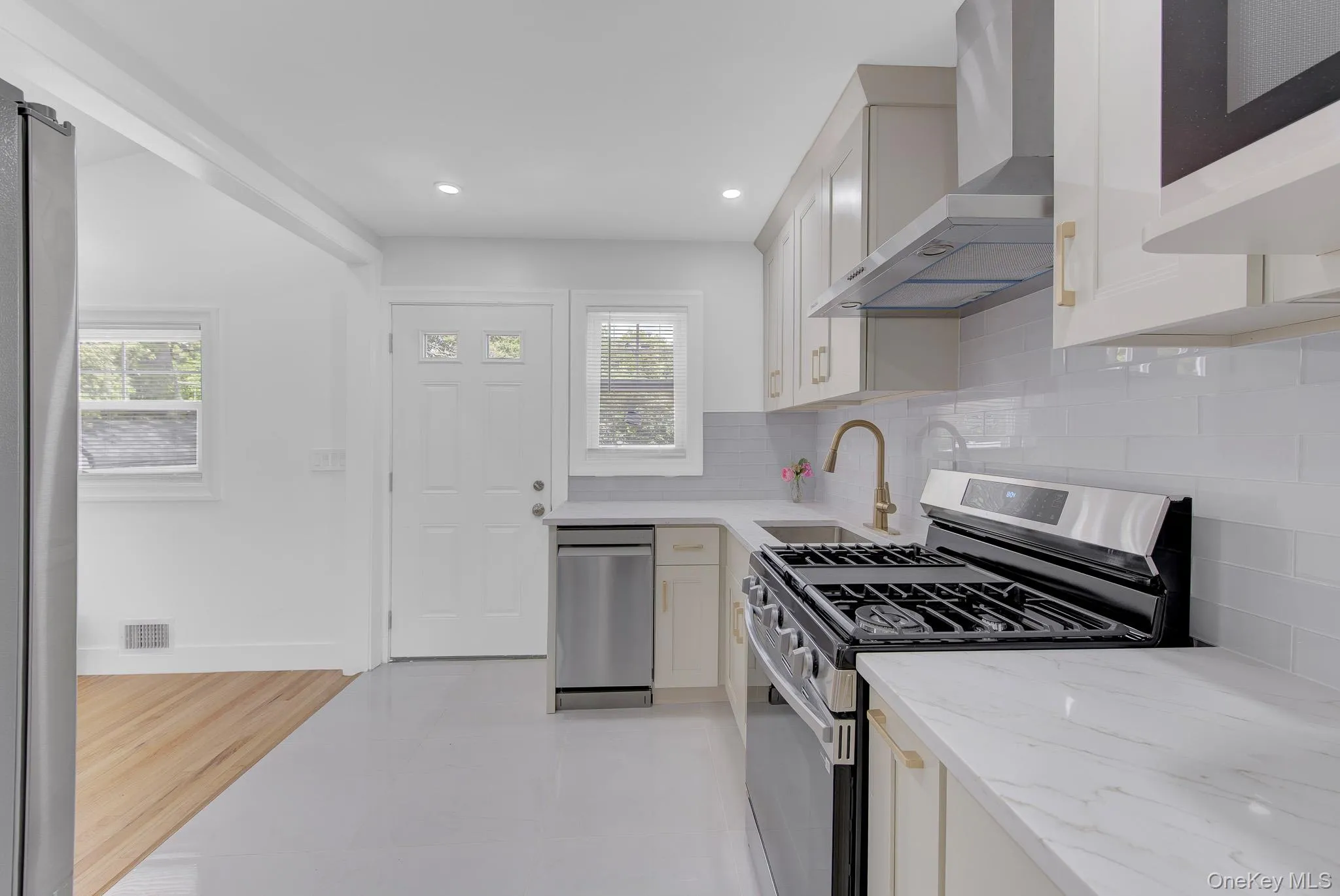 Modern kitchen featuring light-toned cabinetry, stainless steel appliances, a range hood, a brass-finish faucet, and white countertops Modern kitchen featuring light-toned cabinetry, stainless steel appliances, a range hood, a brass-finish faucet, and white countertops