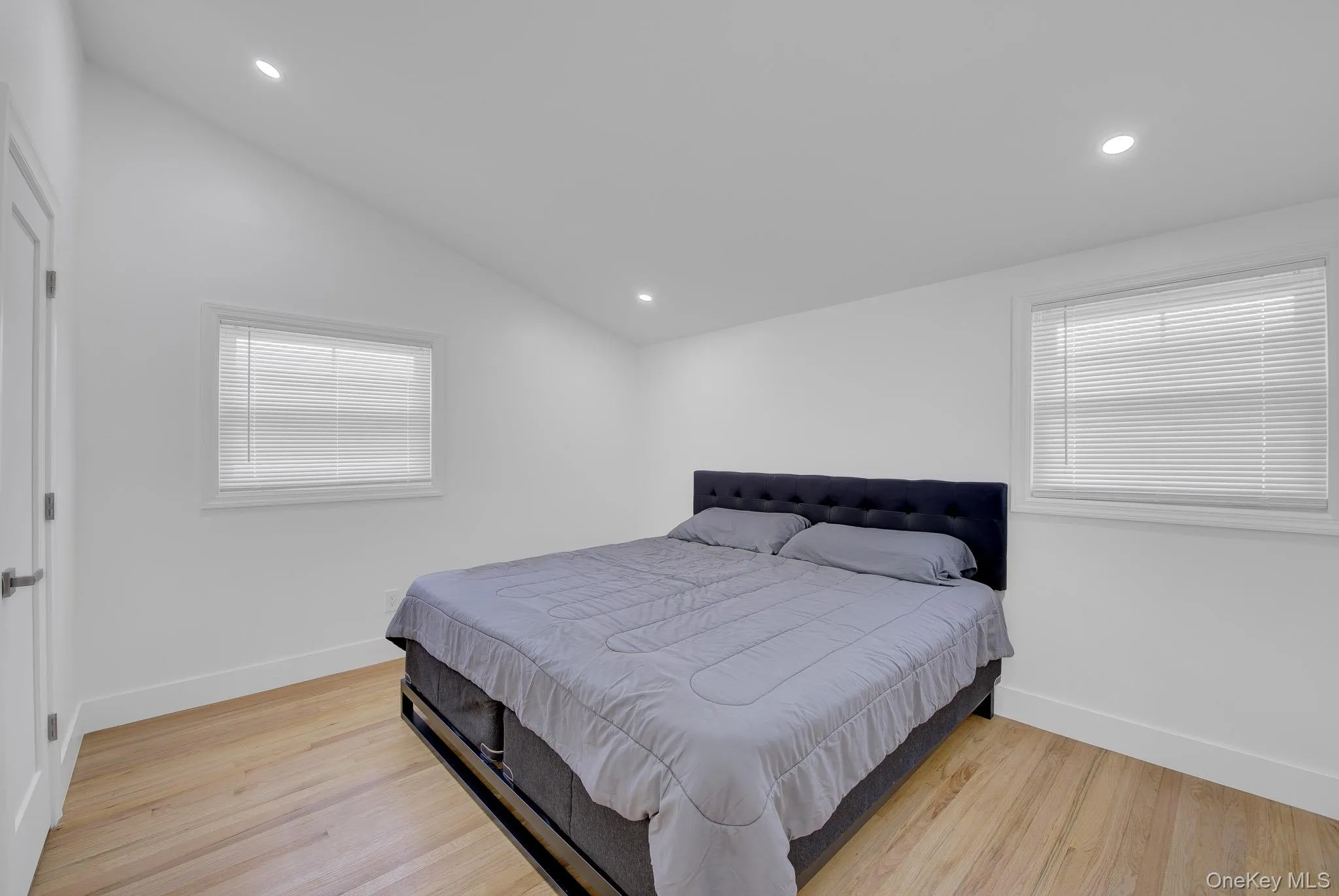 Bright room featuring two windows with horizontal blinds, recessed lighting, wood-finish flooring, and crisp white walls Bright room featuring two windows with horizontal blinds, recessed lighting, wood-finish flooring, and crisp white walls