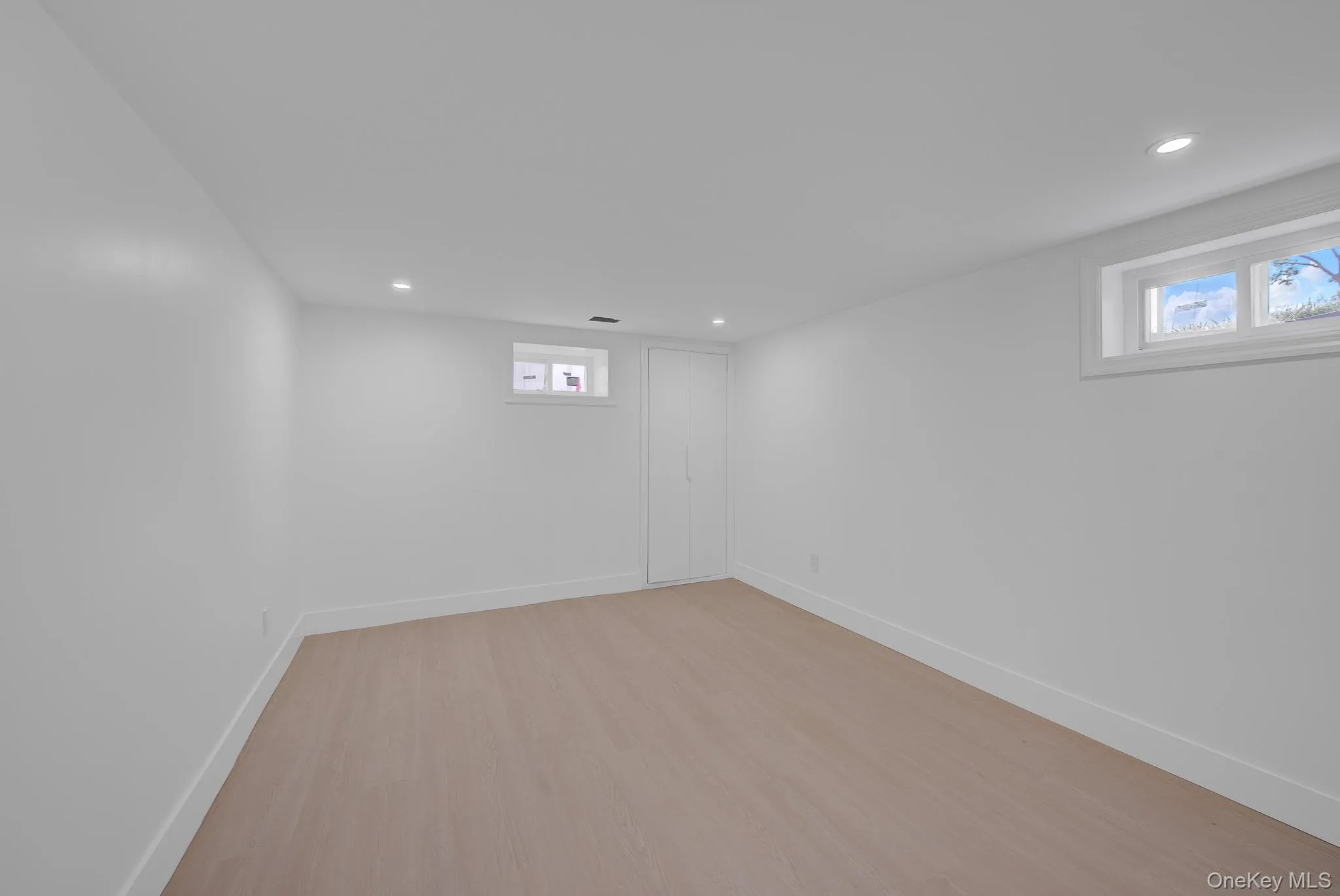 Spacious room featuring wood-finish flooring, recessed lighting, white walls, and two windows Spacious room featuring wood-finish flooring, recessed lighting, white walls, and two windows
