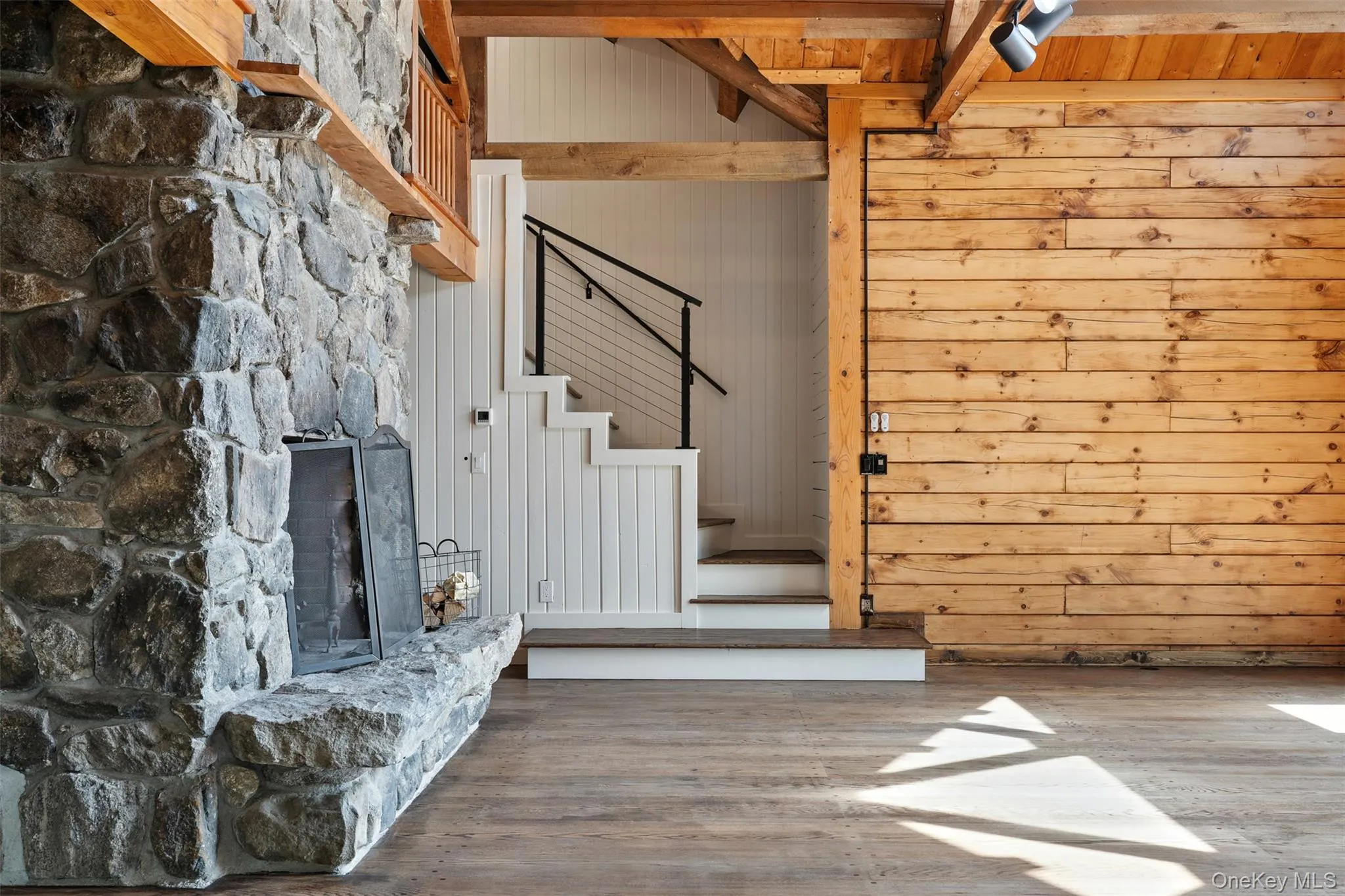 Stairway with wood finished floors, a stone fireplace, beamed ceiling, and wooden walls Stairway with wood finished floors, a stone fireplace, beamed ceiling, and wooden walls