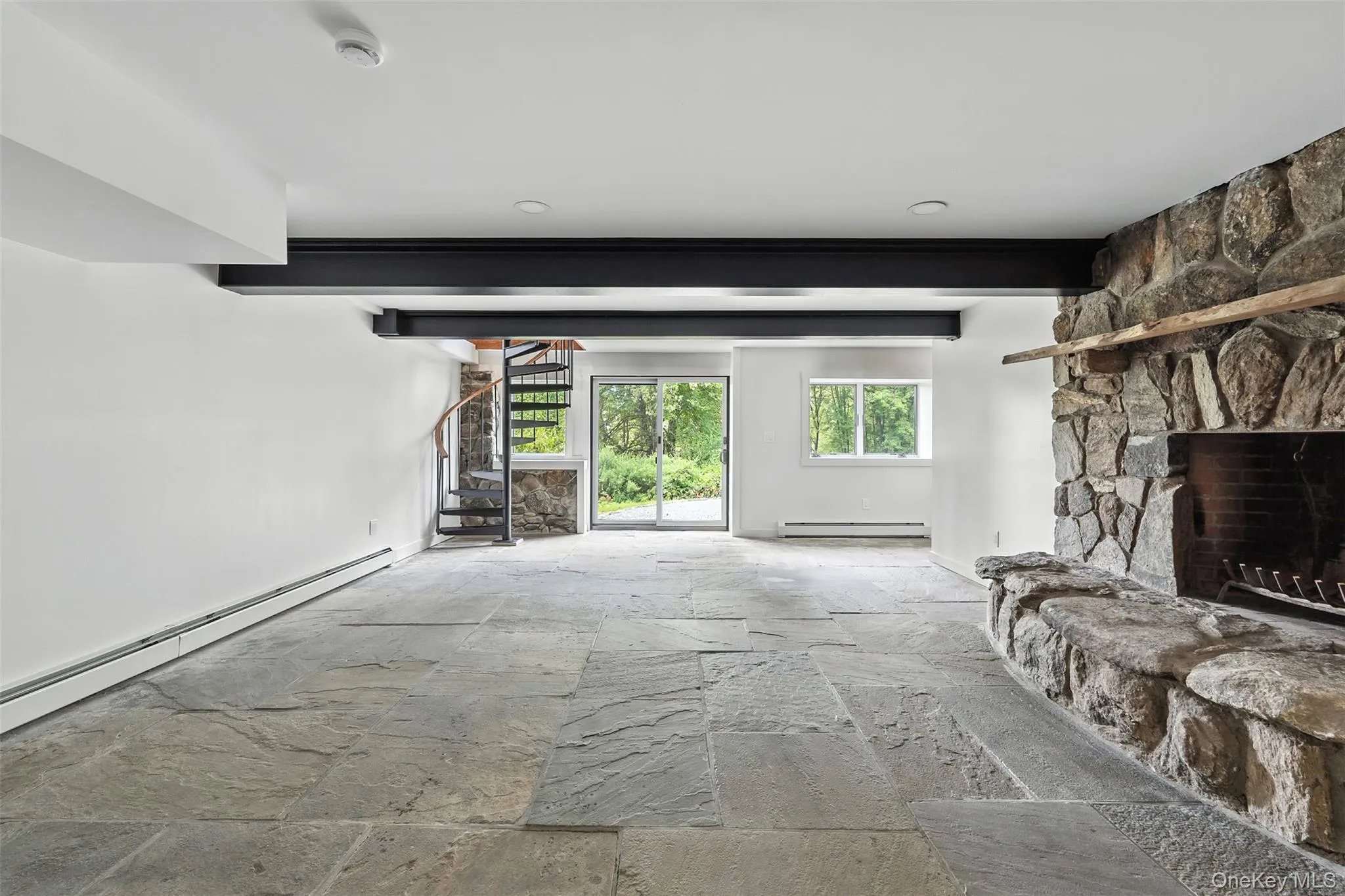 Living area with a fireplace, stone tile flooring, stairs, and a baseboard heating unit Living area with a fireplace, stone tile flooring, stairs, and a baseboard heating unit