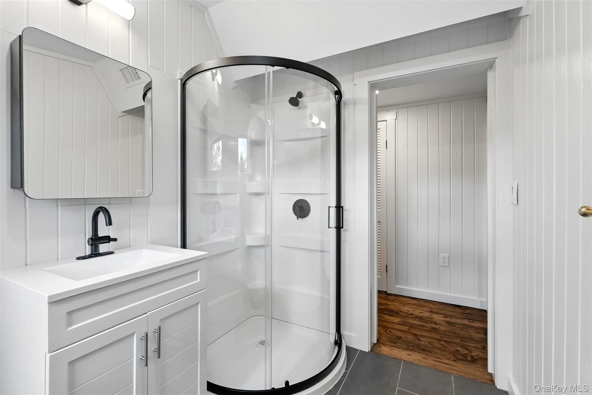 Full bath with dark tile patterned flooring, vanity, a shower stall, and wood walls Full bath with dark tile patterned flooring, vanity, a shower stall, and wood walls