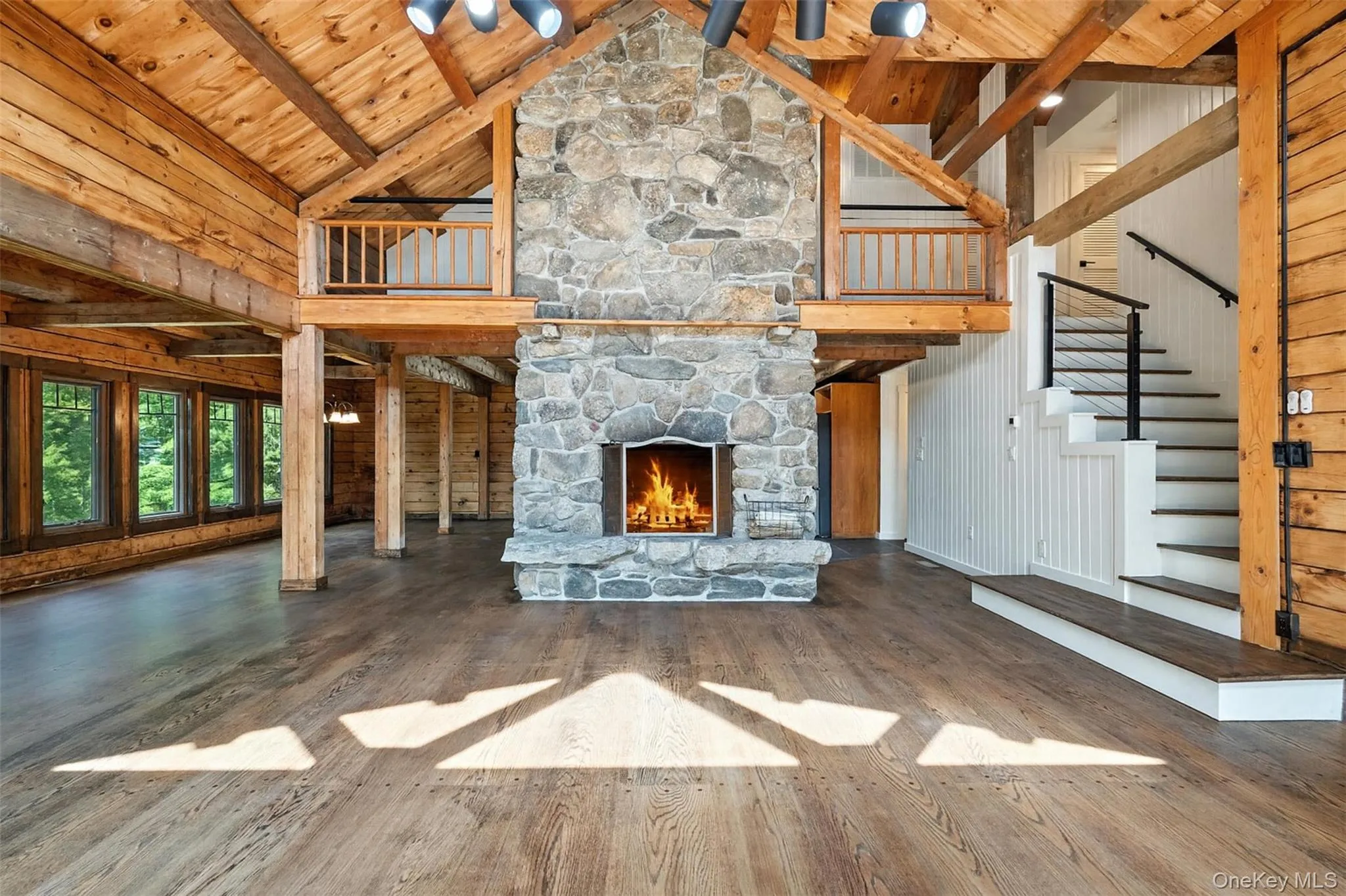 Unfurnished living room with high vaulted ceiling, wood walls, wood finished floors, a wood ceiling with exposed beams, and a stone fireplace Unfurnished living room with high vaulted ceiling, wood walls, wood finished floors, a wood ceiling with exposed beams, and a stone fireplace