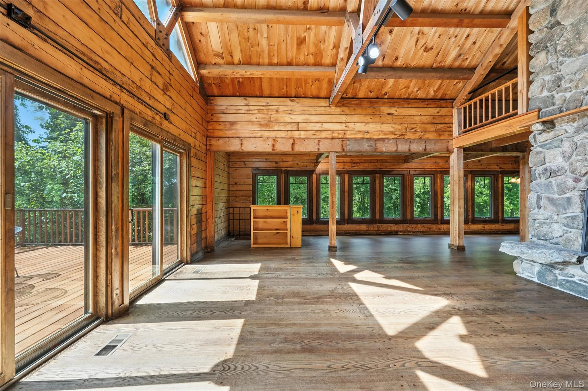 Unfurnished living room with wooden walls, high vaulted ceiling, wood-type flooring, a wood ceiling with exposed beams, and plenty of natural light Unfurnished living room with wooden walls, high vaulted ceiling, wood-type flooring, a wood ceiling with exposed beams, and plenty of natural light